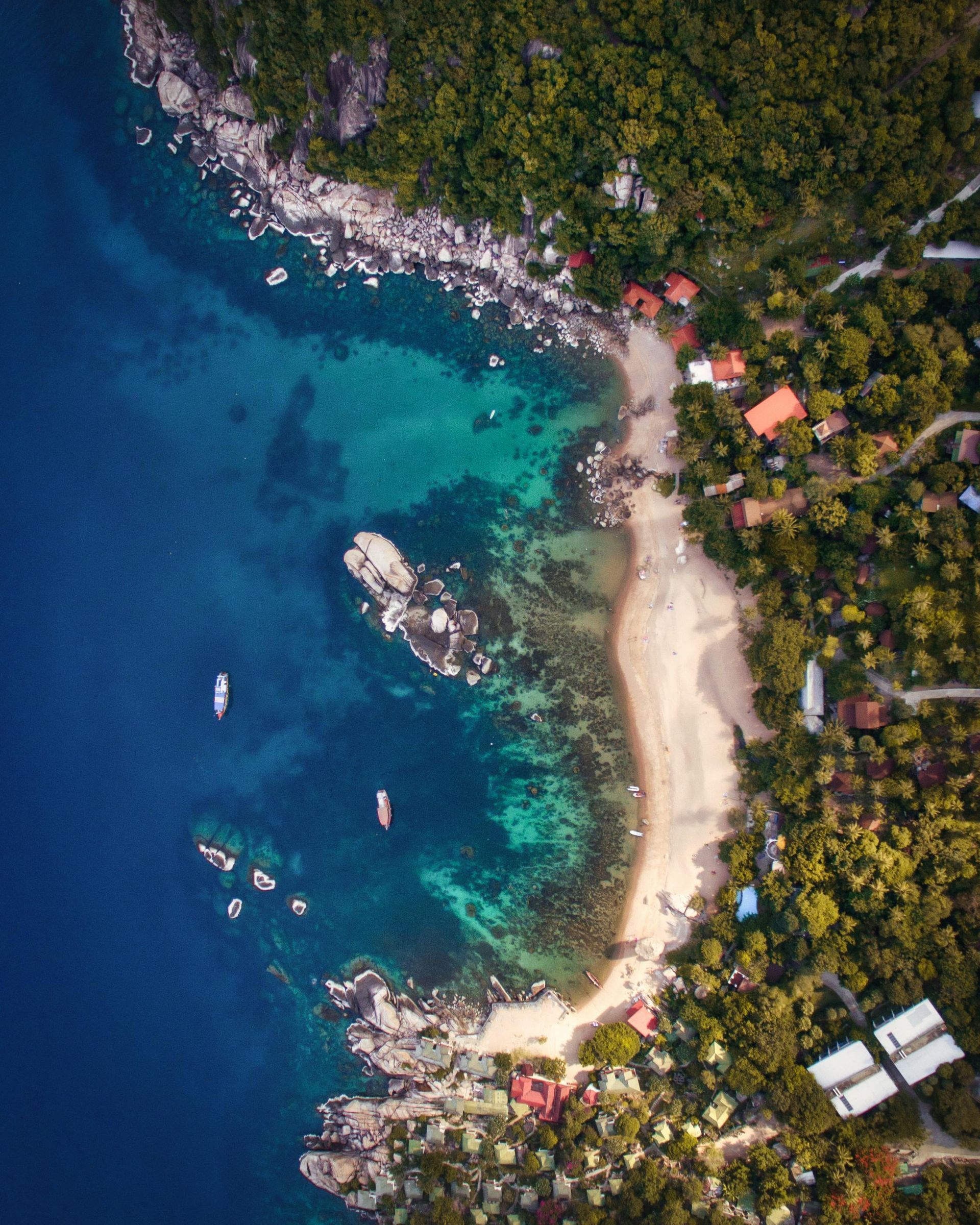 An aerial view of a beach surrounded by trees and a body of water in Thailand.