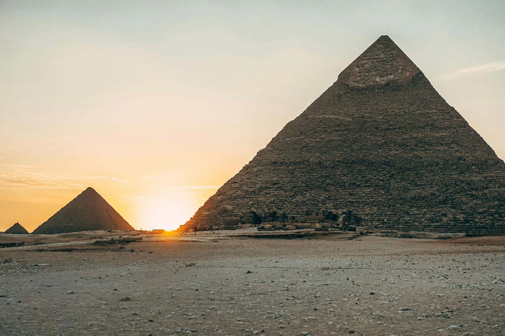 The sun is setting behind two pyramids in the desert in Egypt.