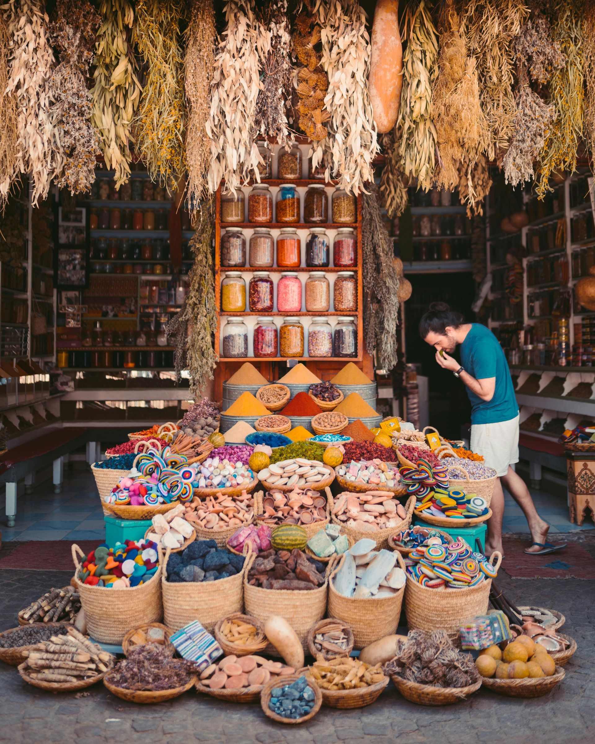 A man is standing in front of a store filled with baskets of food in Morocco.