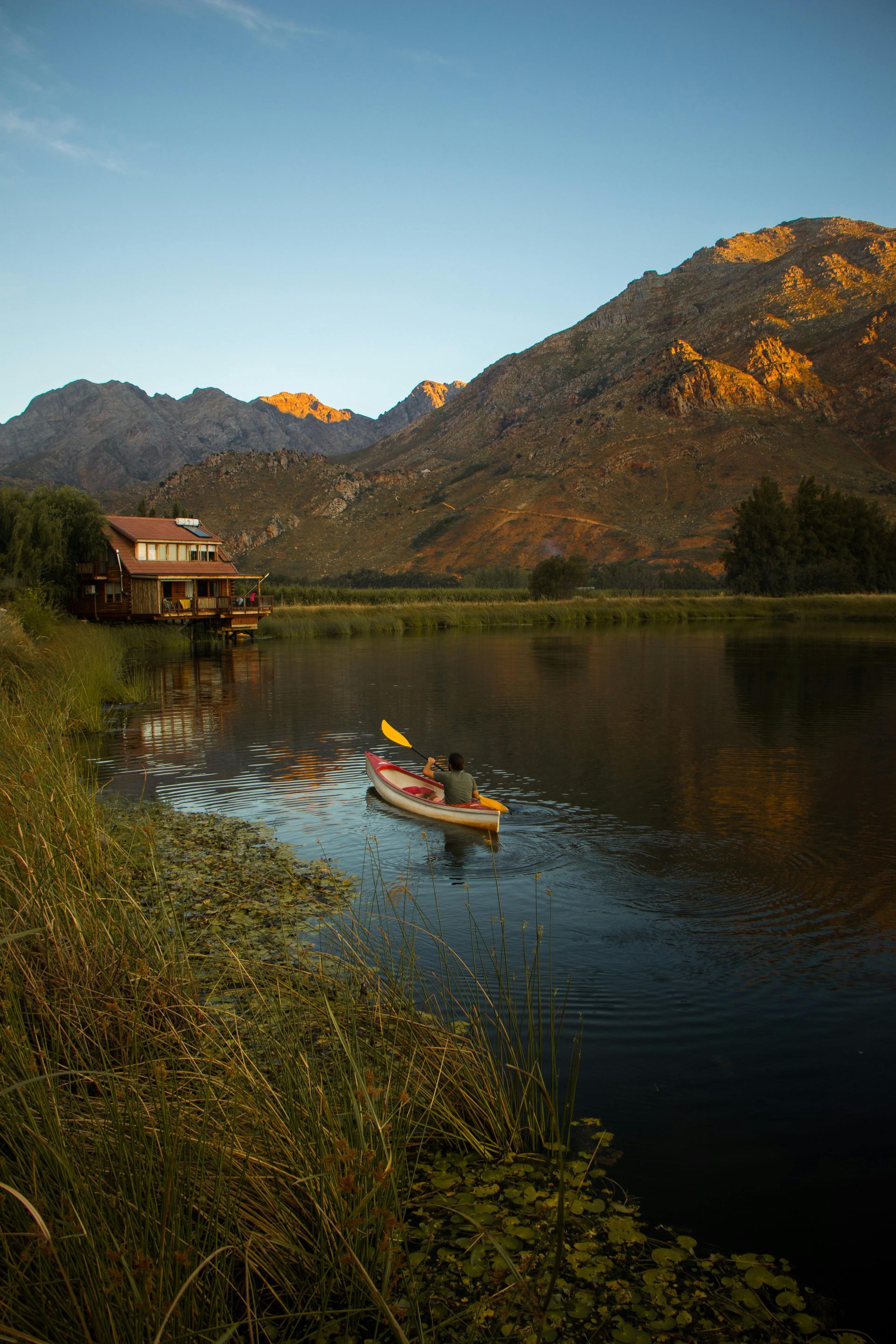 A person is paddling a kayak on a lake with mountains in the background in South Africa.