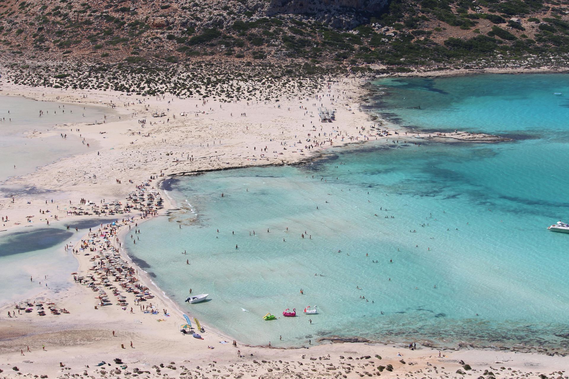 An aerial view of a beach with boats in the water in Crete, Greece.