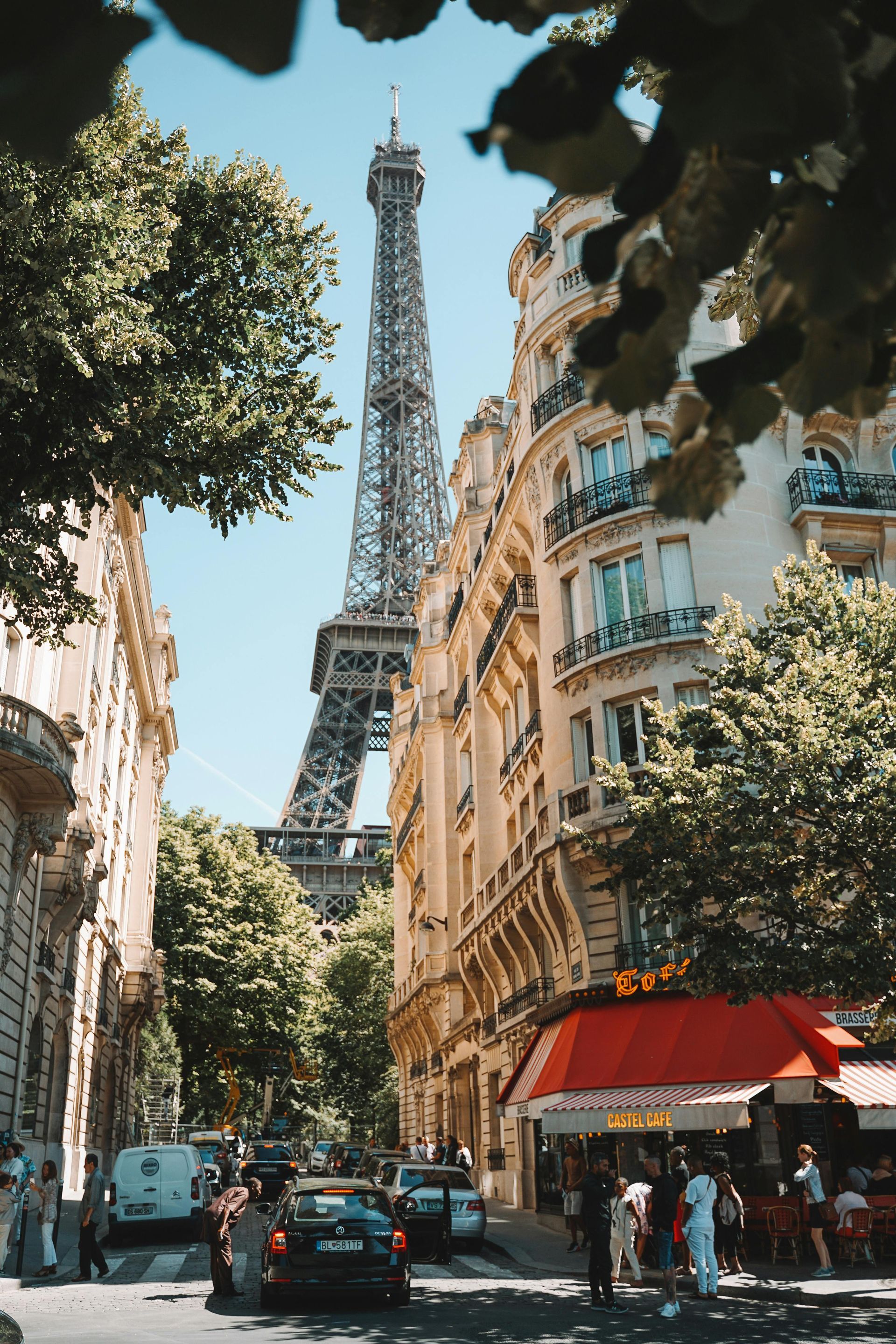 The eiffel tower is visible through the trees in the middle of a city street.