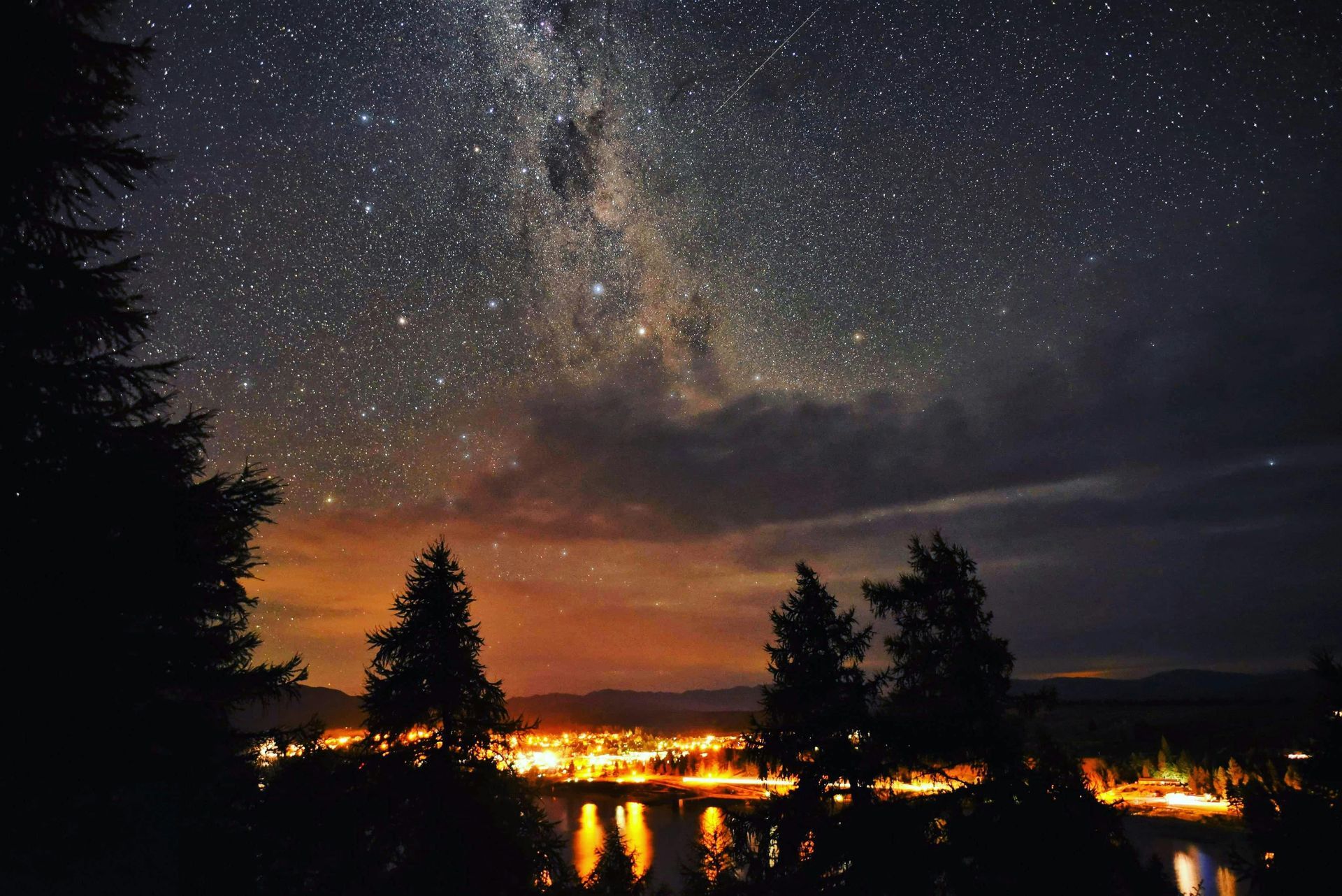 A starry night sky over a city with trees in the foreground in New Zeland.