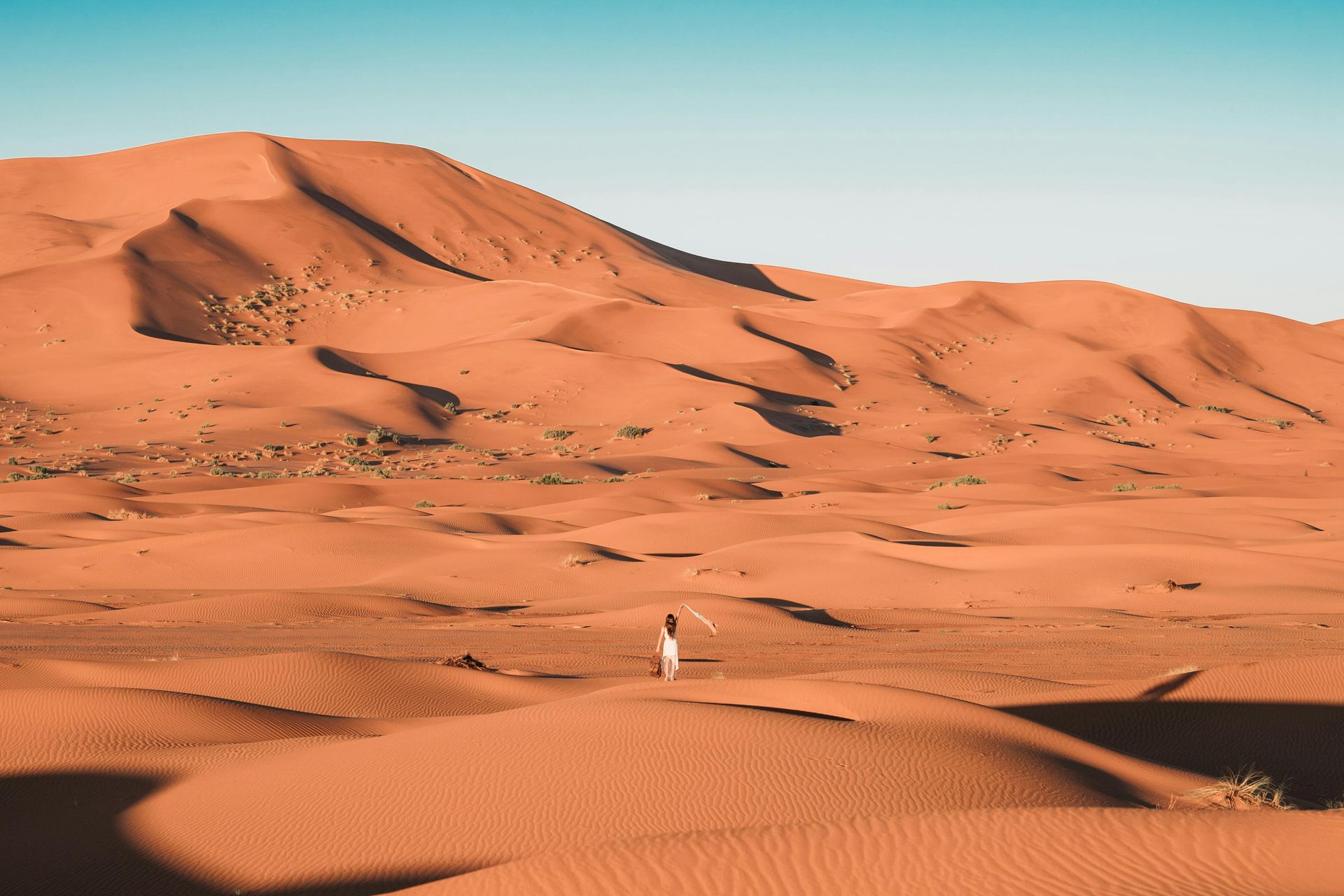 A person is standing in the middle of a Sahara desert with mountains in the background in Morocco.