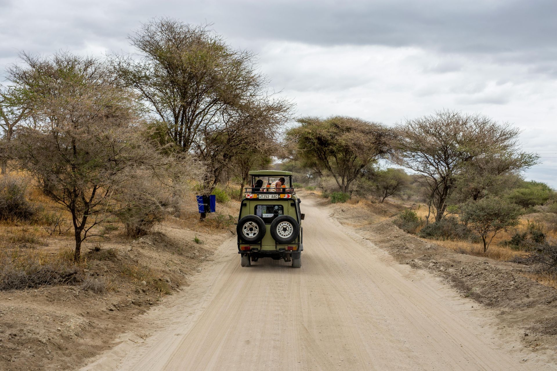 A green jeep is driving down a dirt road in Kenya Africa.