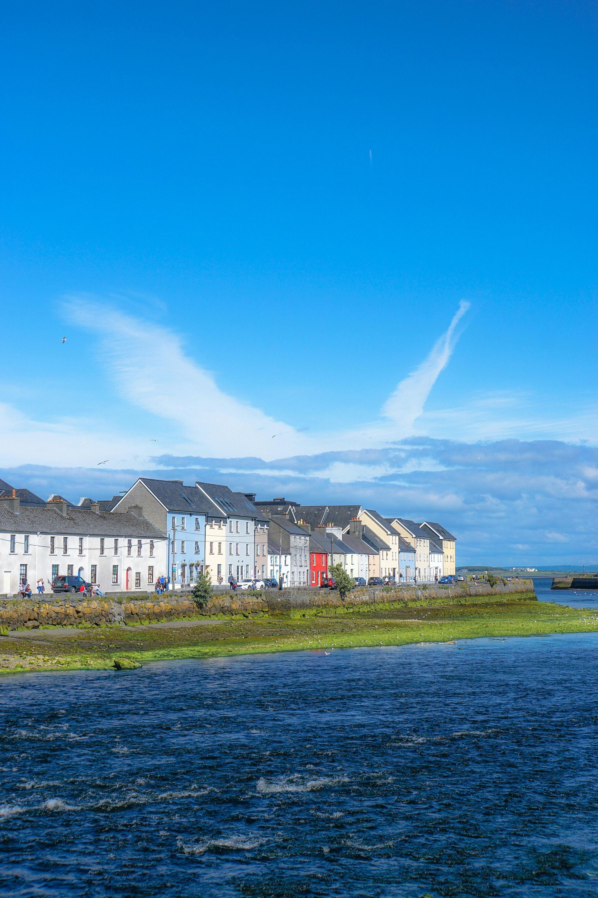 A row of houses next to a body of water on a sunny day in Ireland.