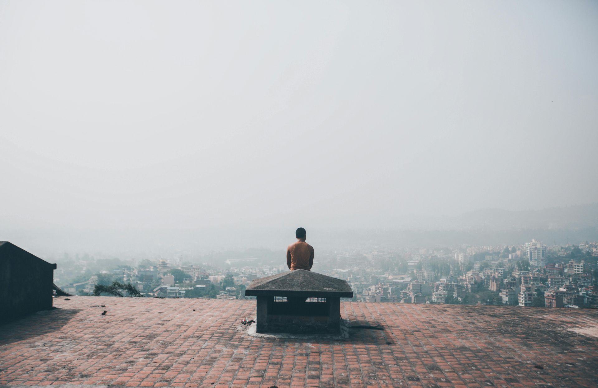 A man is sitting on top of a brick roof overlooking a city in Bhutan.