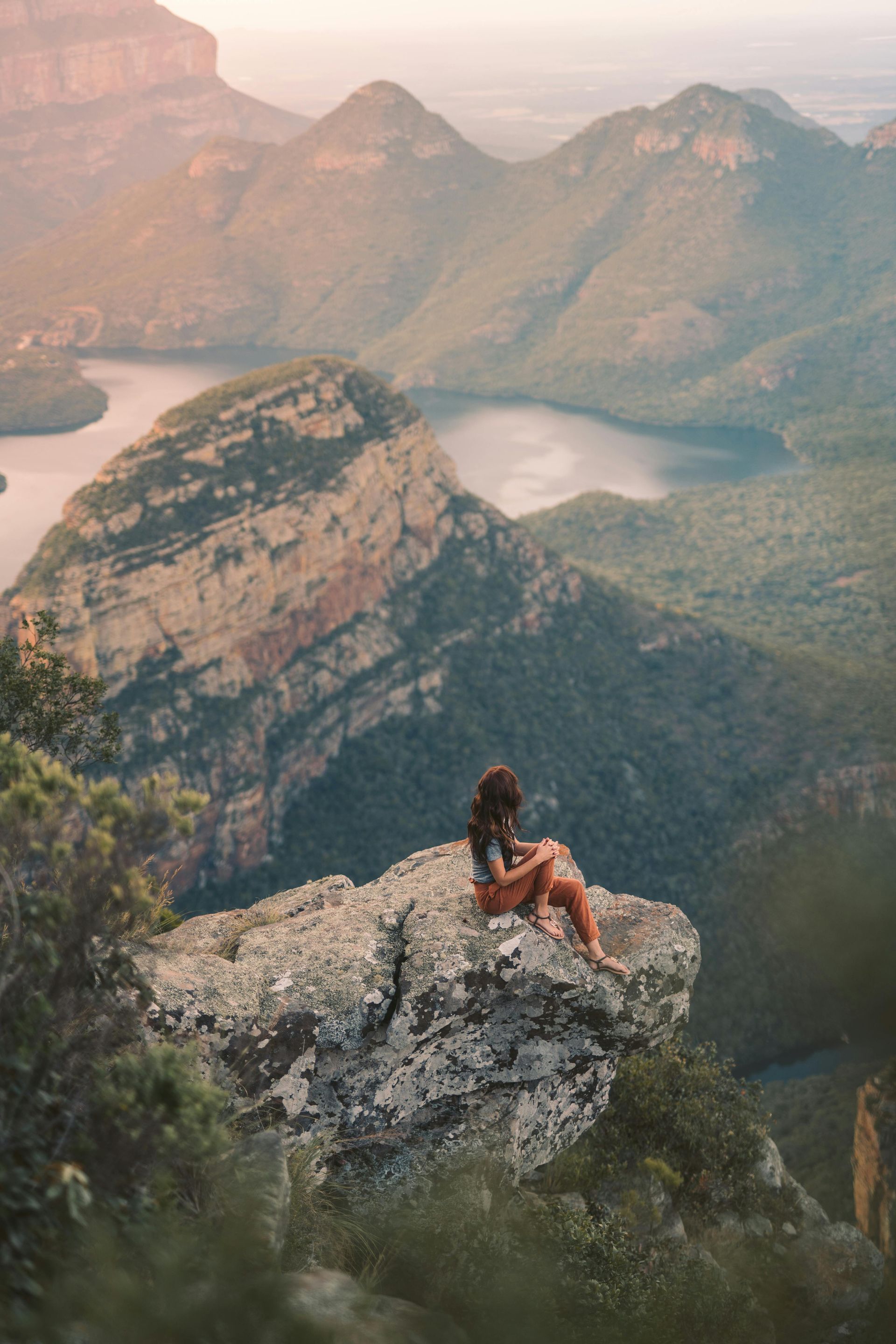 A woman is sitting on the edge of a cliff overlooking a lake in South Africa.