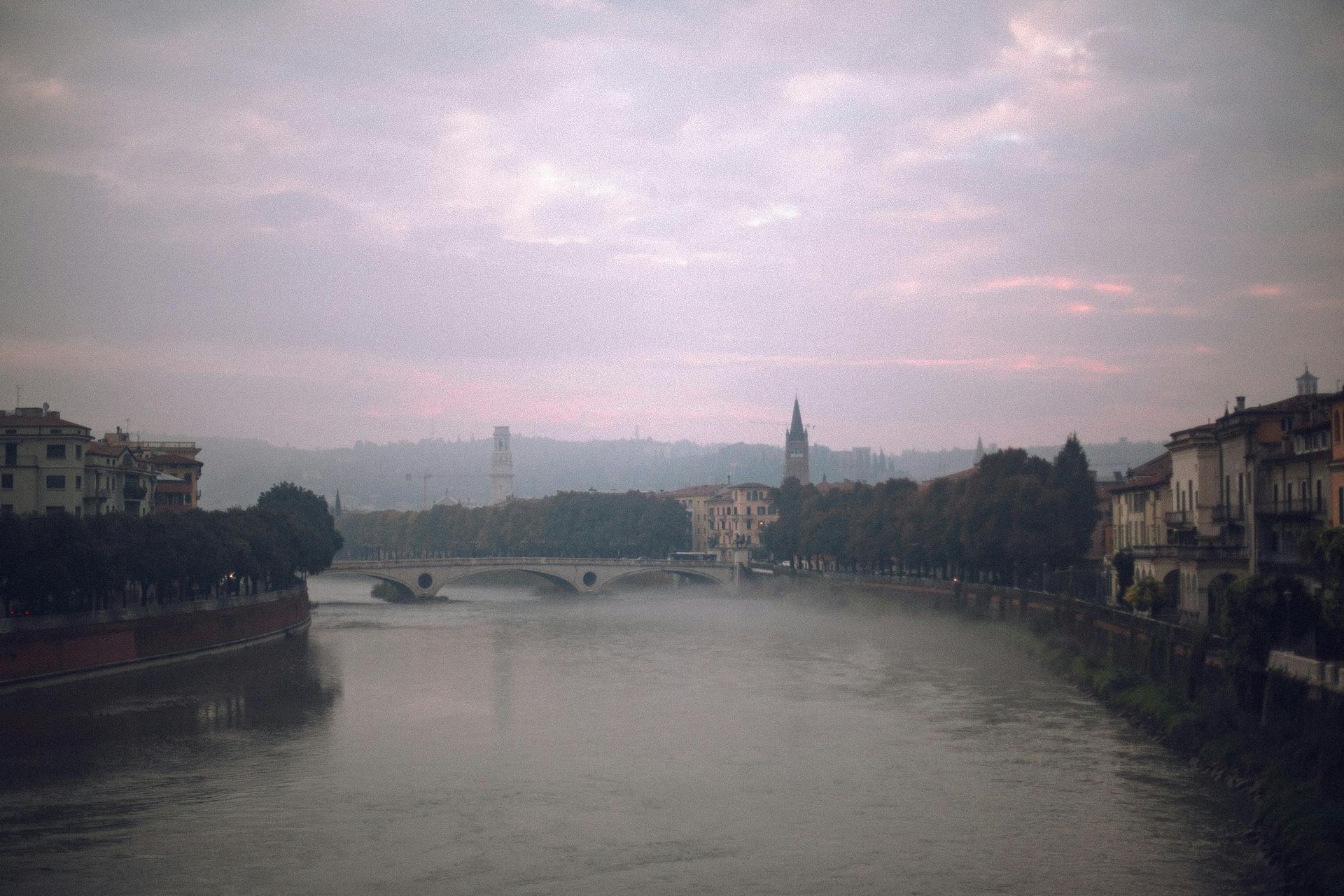 A river with a bridge in the distance and Verona, Italy in the background