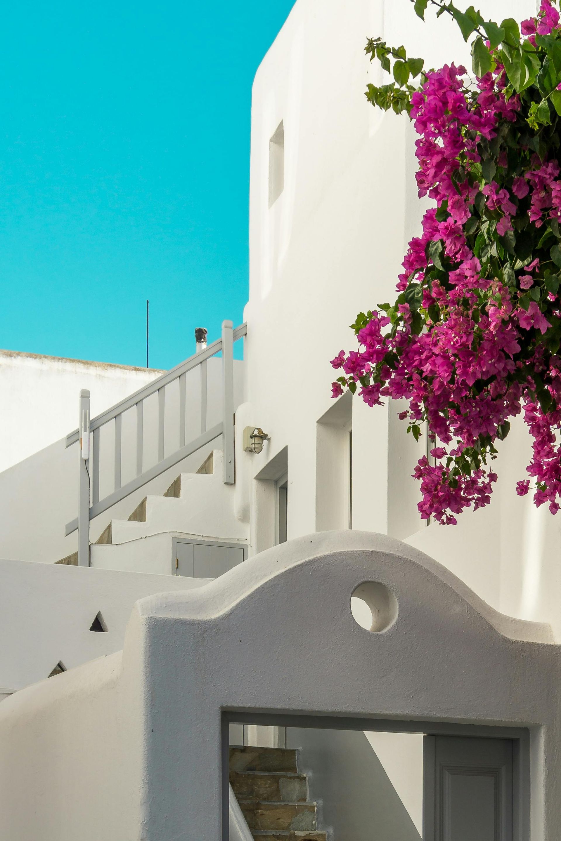 A white building with purple flowers in front of it in Mykonos, Greece.