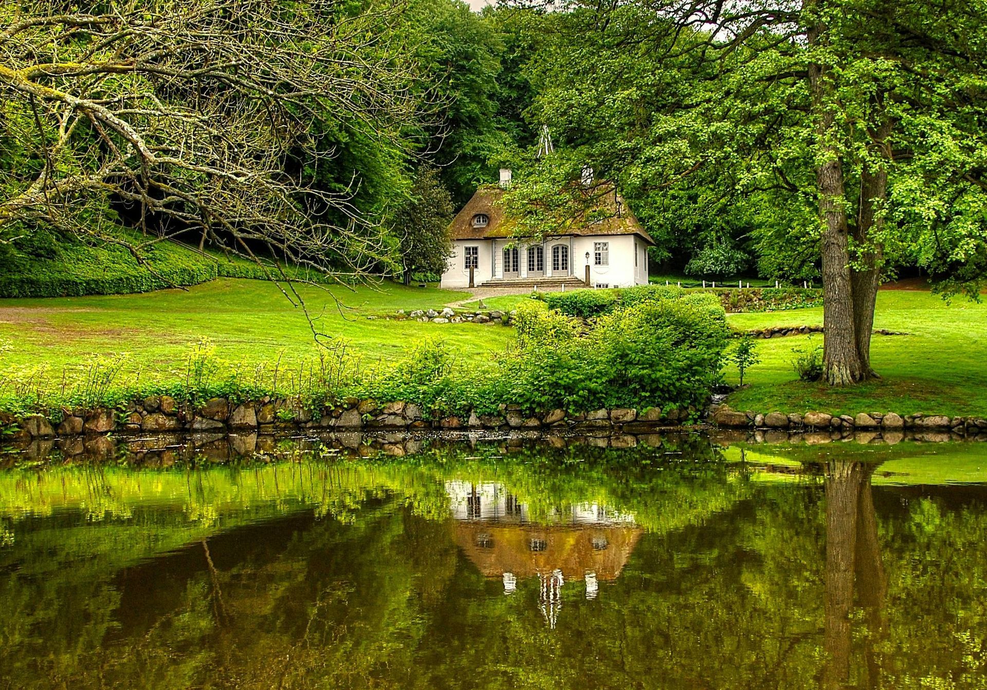 A house is reflected in a pond with trees in the background in Denmark.