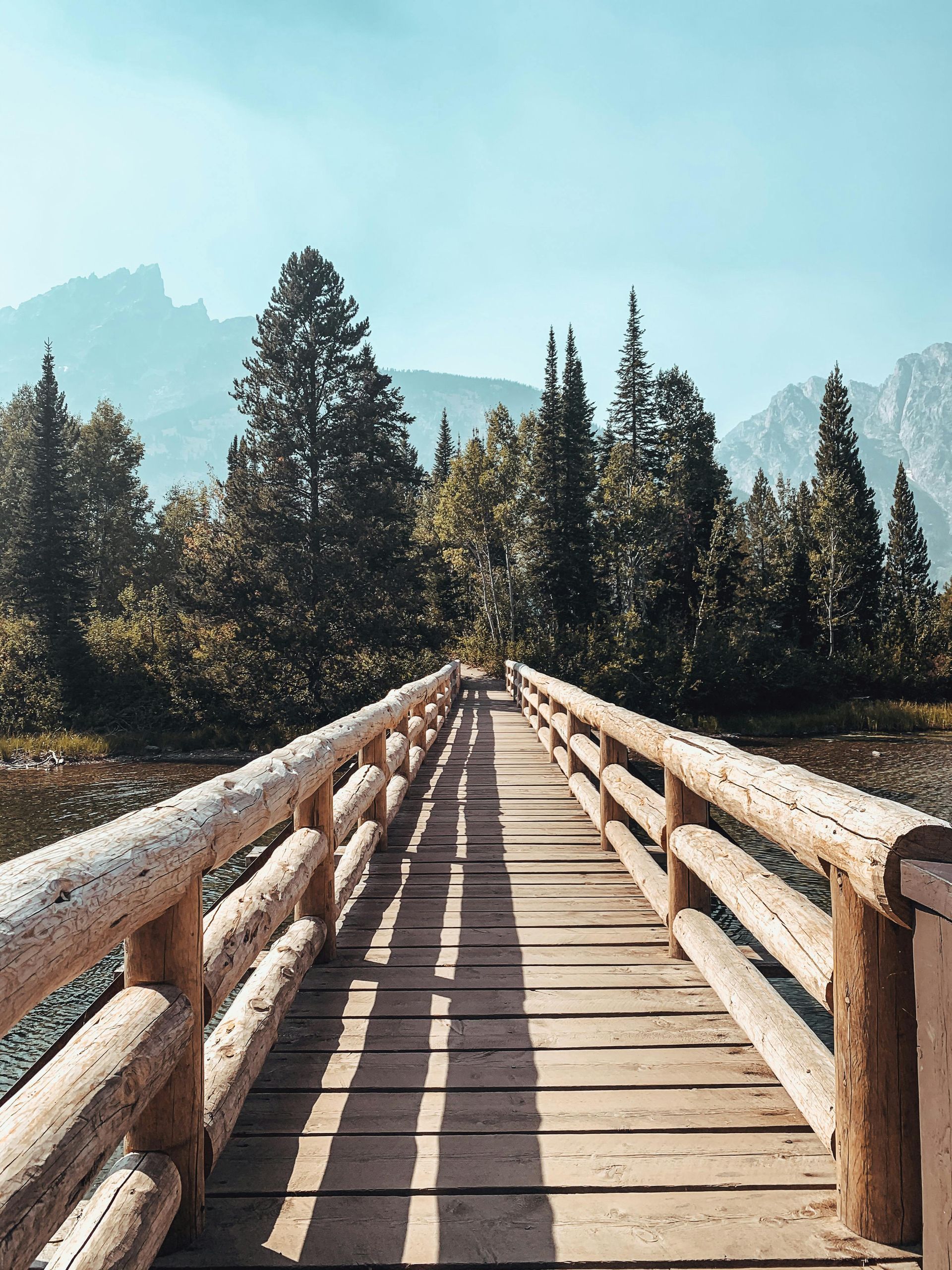 A wooden bridge over a lake surrounded by trees and mountains in Montana.