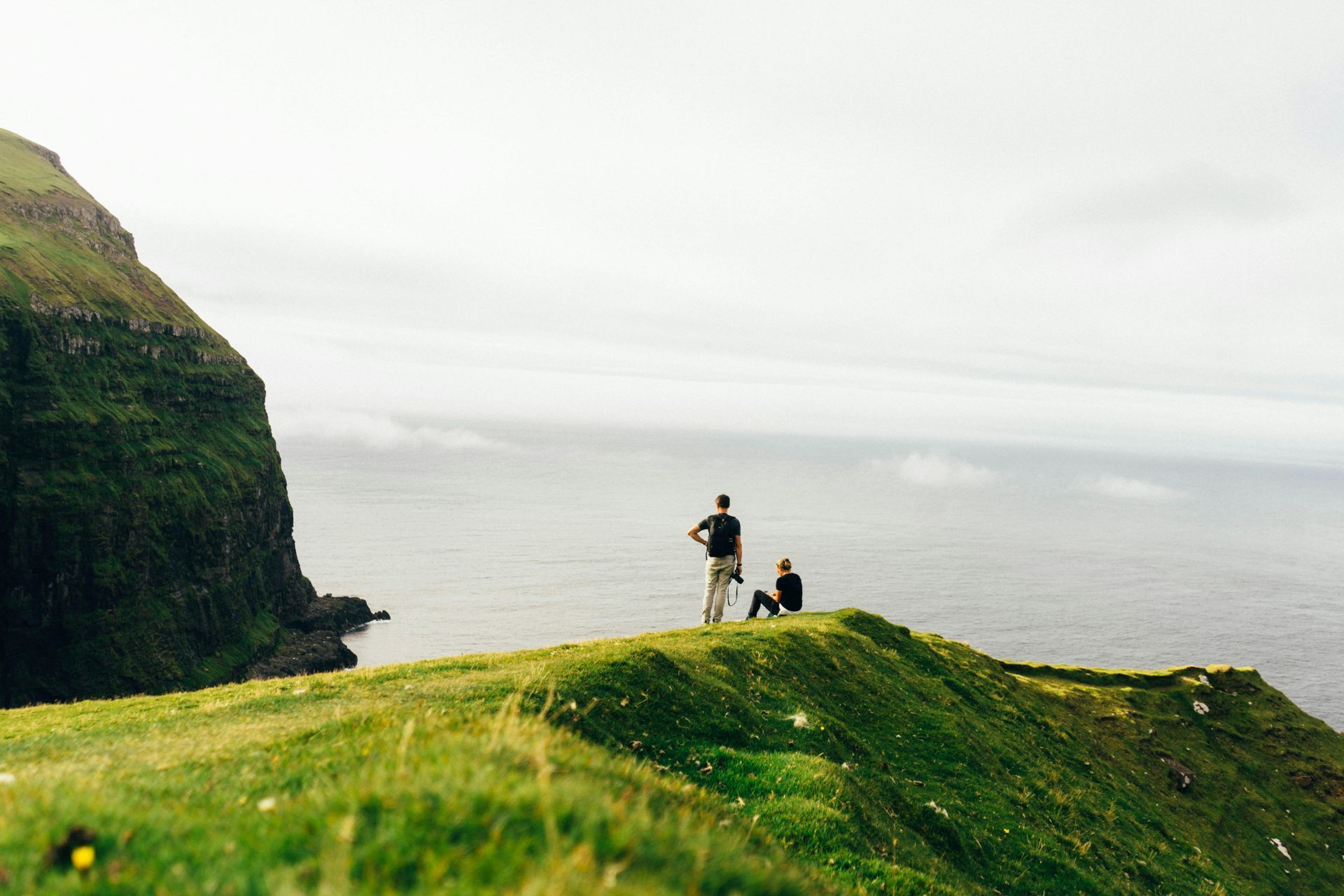 A couple of people standing on top of a cliff overlooking the ocean in Denmark.