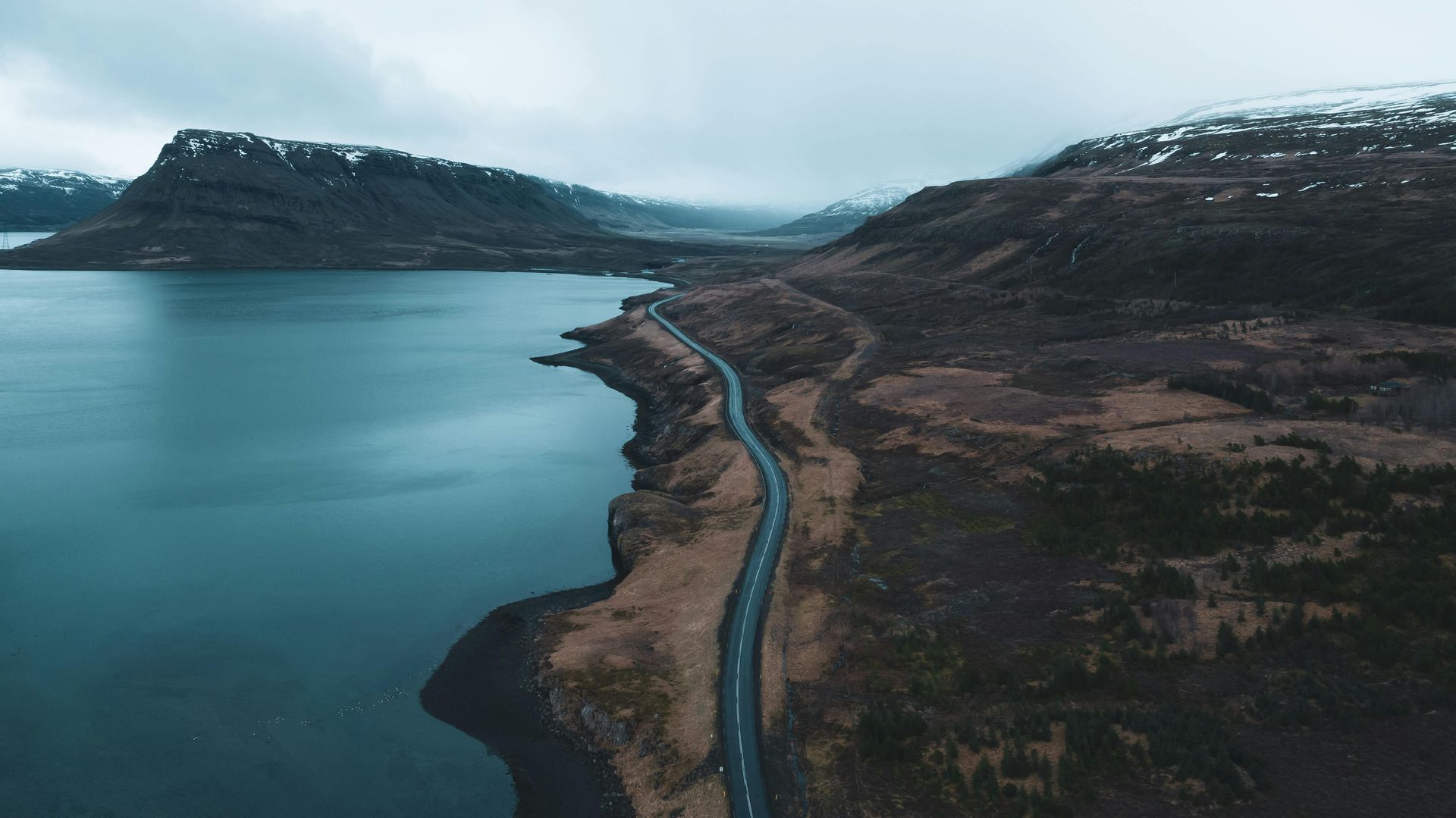 An aerial view of a road going through a lake surrounded by mountains in Iceland.