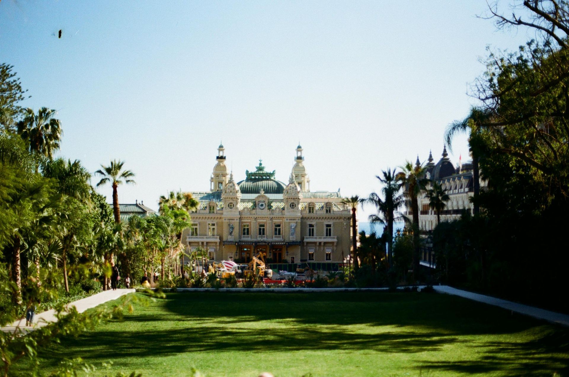 A large building is surrounded by trees and grass in a park in Monaco.