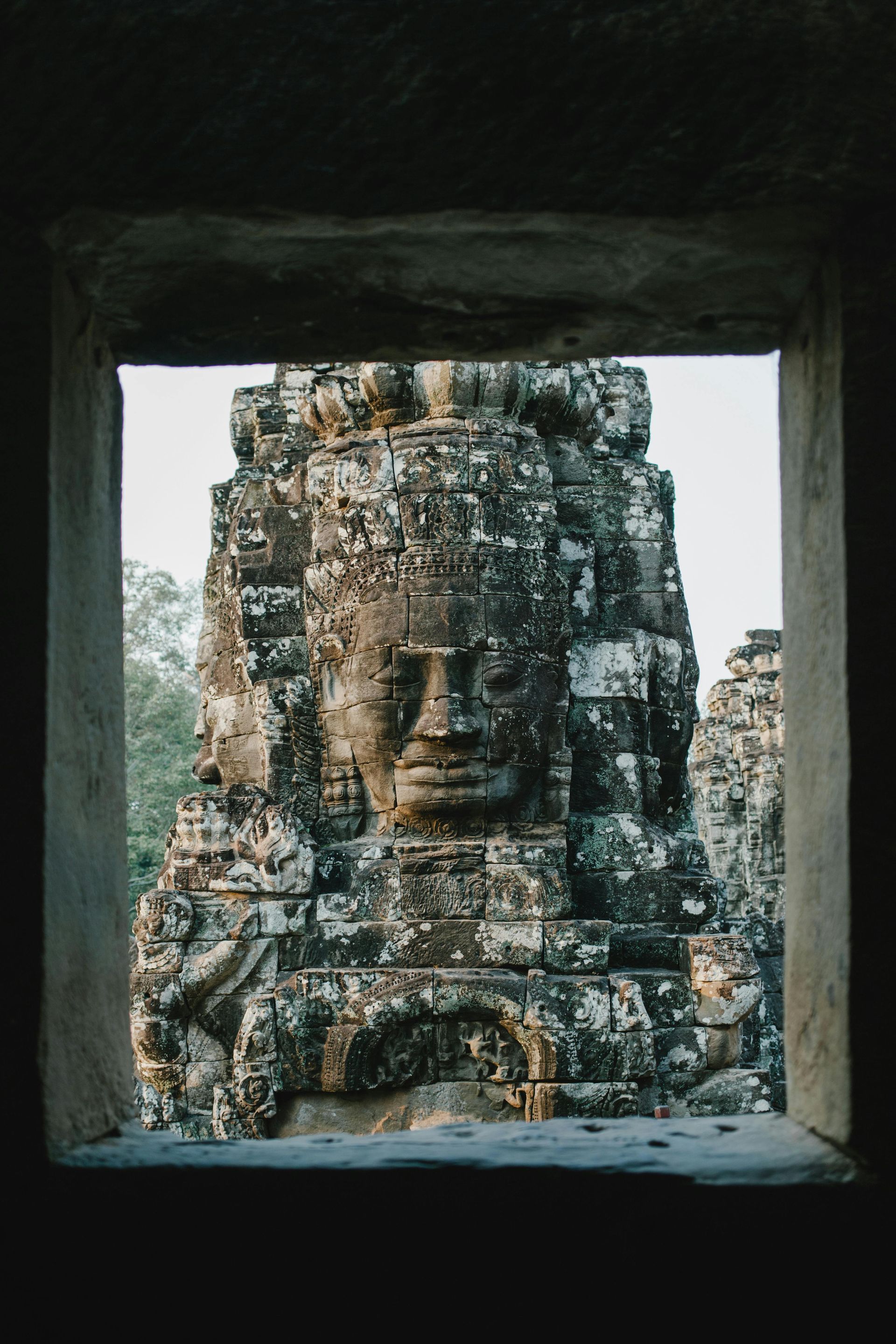 A large stone statue of a face is visible through a window in Cambodia.