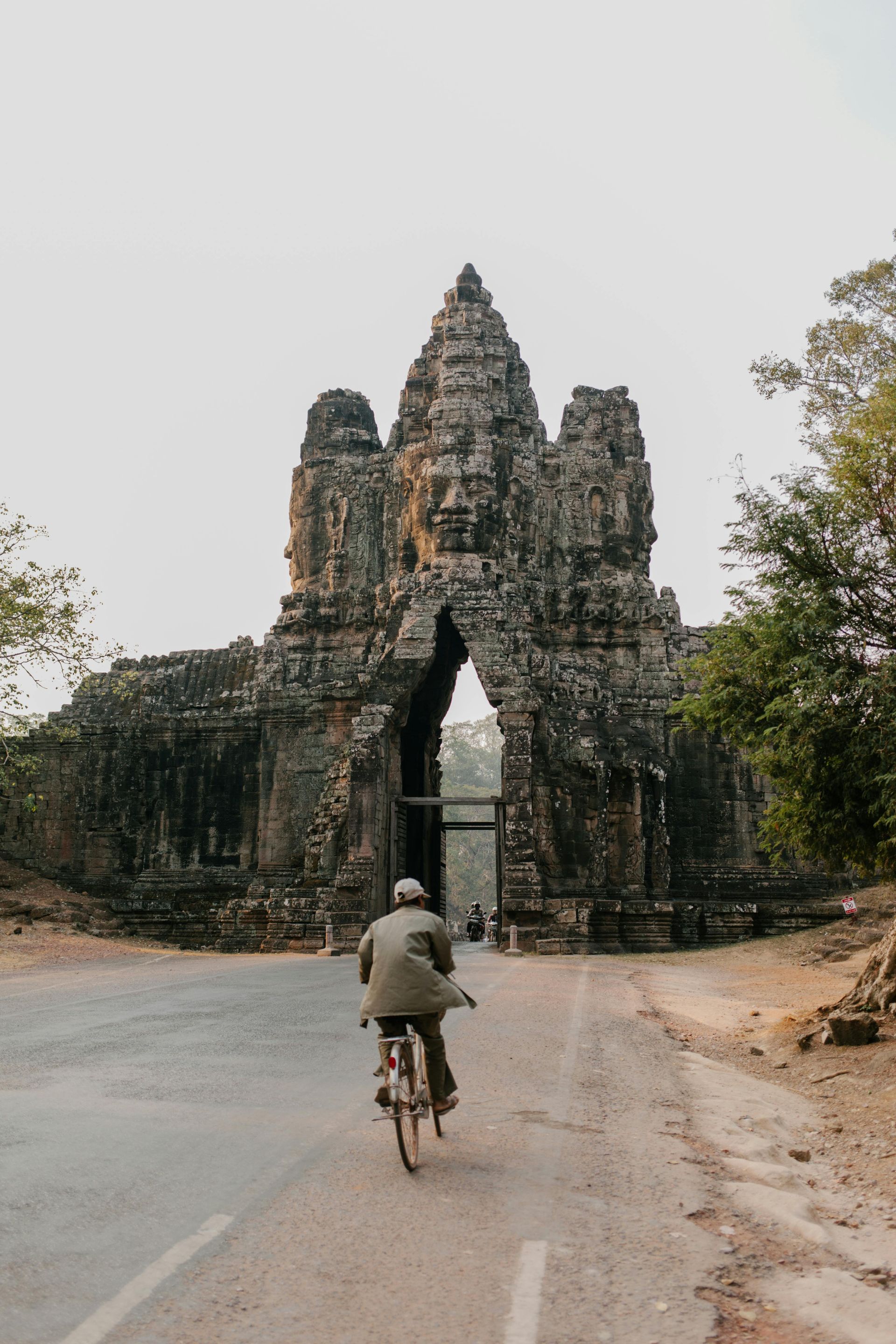 A man is riding a bike down a road in front of a temple in Cambodia.