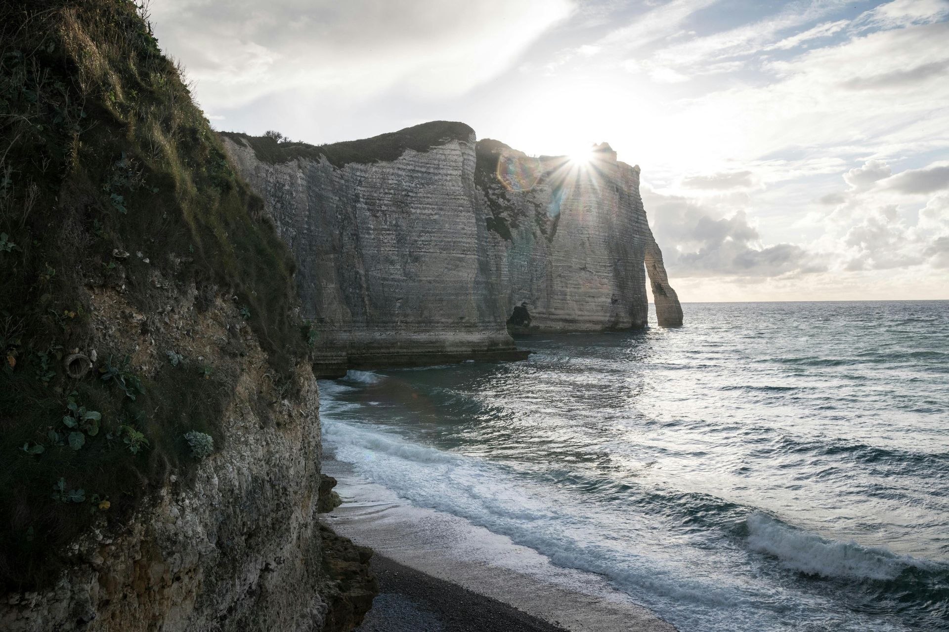 The sun is shining through the clouds over the ocean in Normandy, France.