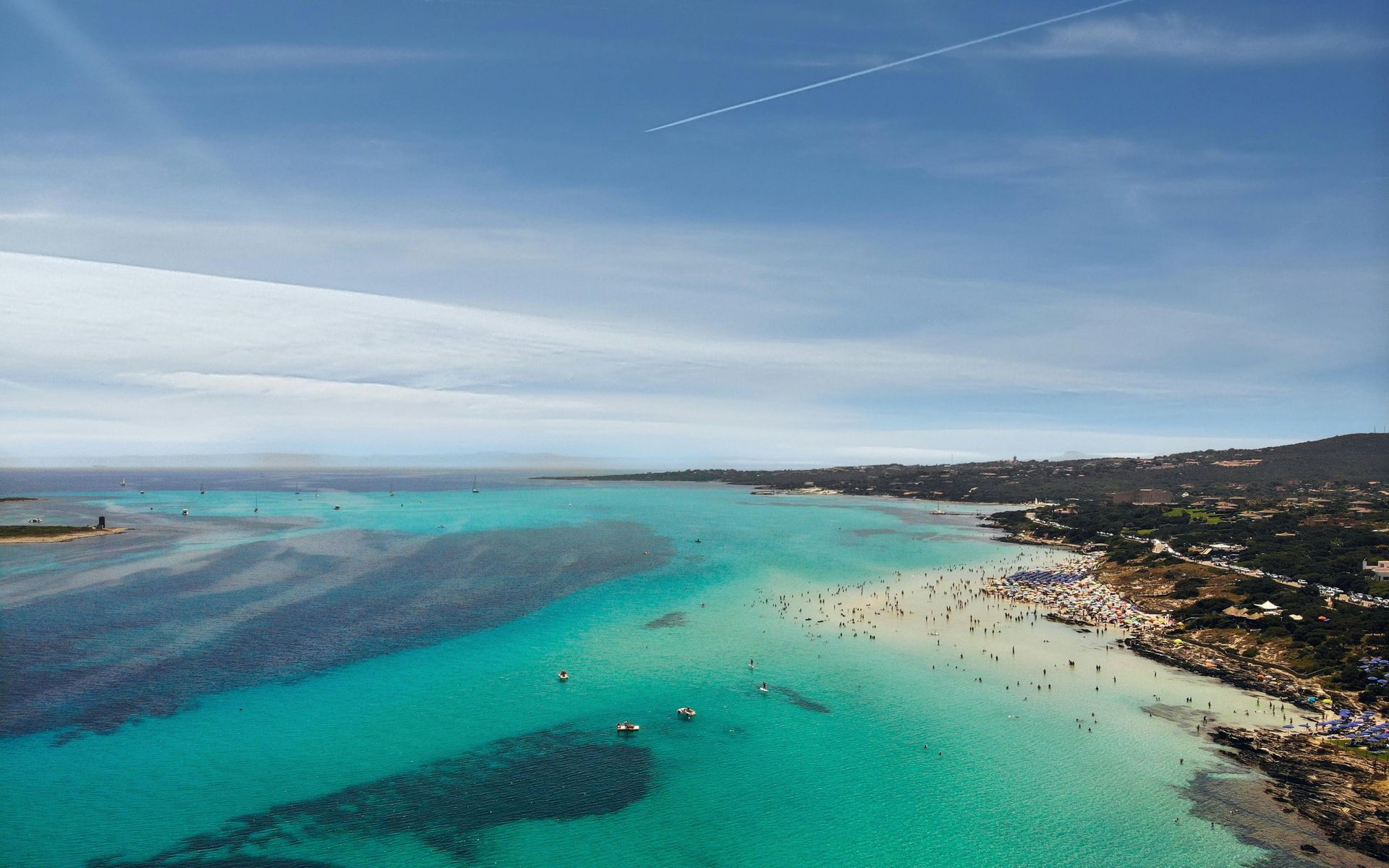 An aerial view of a beach with a lot of people swimming in the ocean in Sardinia, Italy.