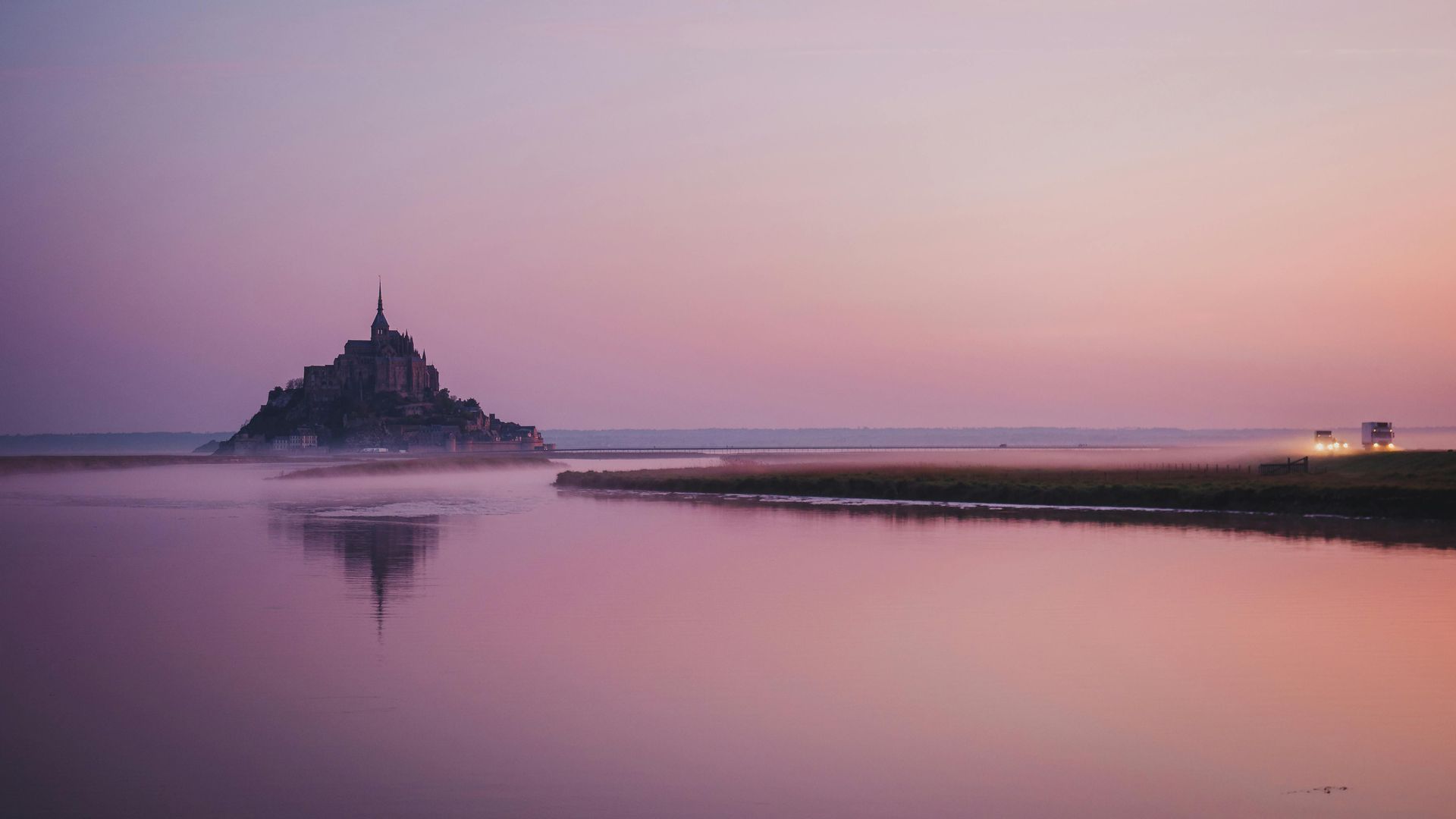 A small island with the castle Mont Saint-Michel on top of it in Normandy, France at sunset.