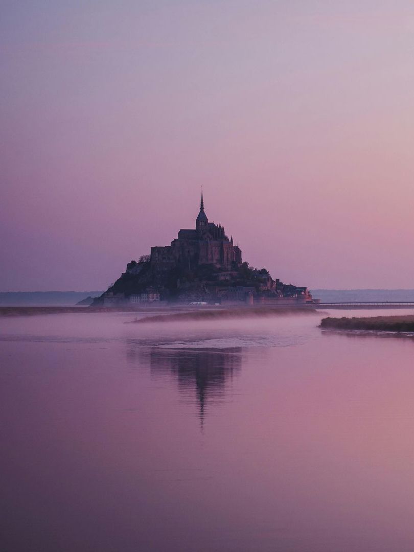 A small island with the castle Mont Saint-Michel in the middle of a body of water at sunset in Normandy, France.