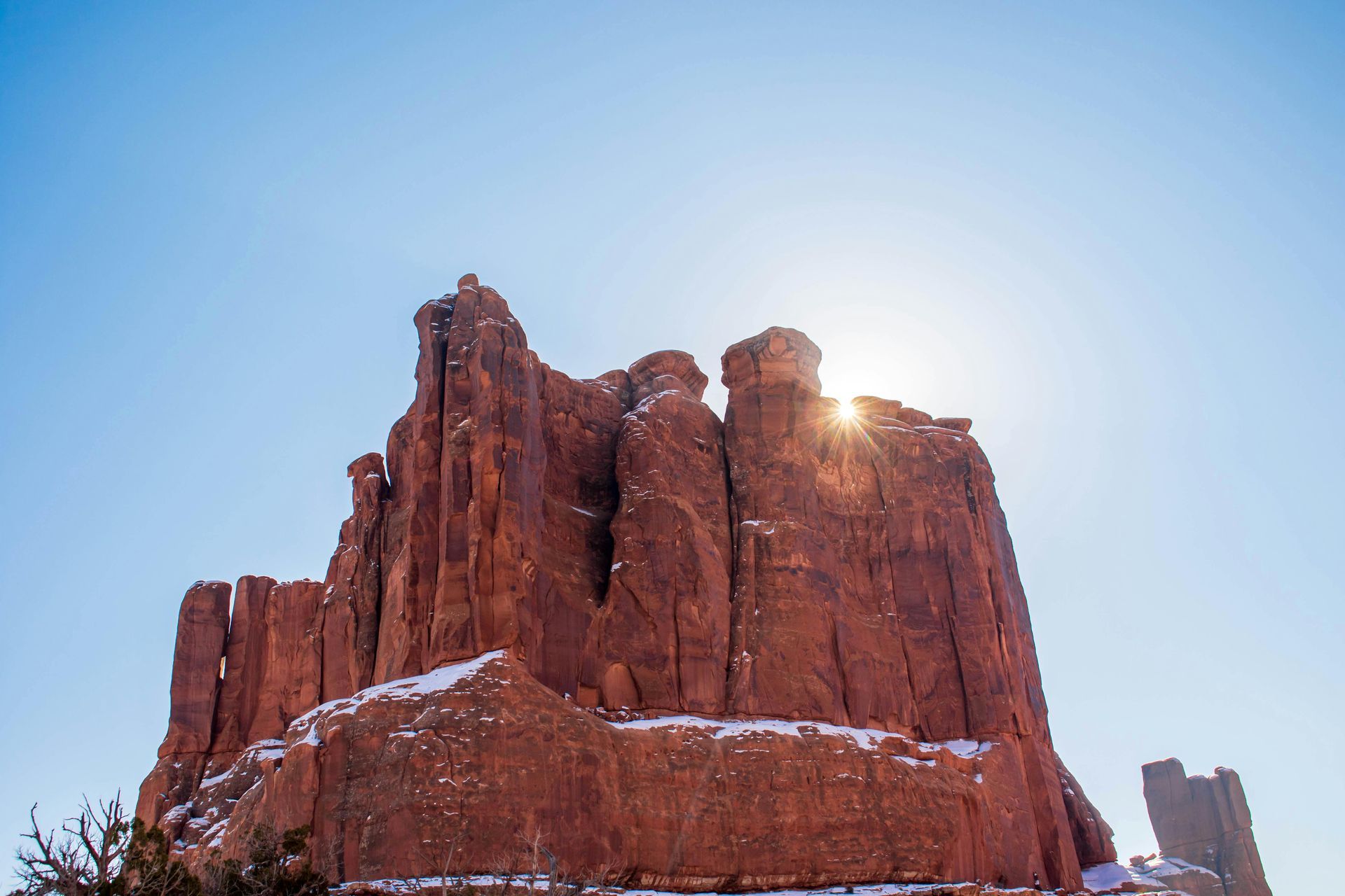 The sun is shining on a large rock formation in the desert at Arches National Park in Utah.