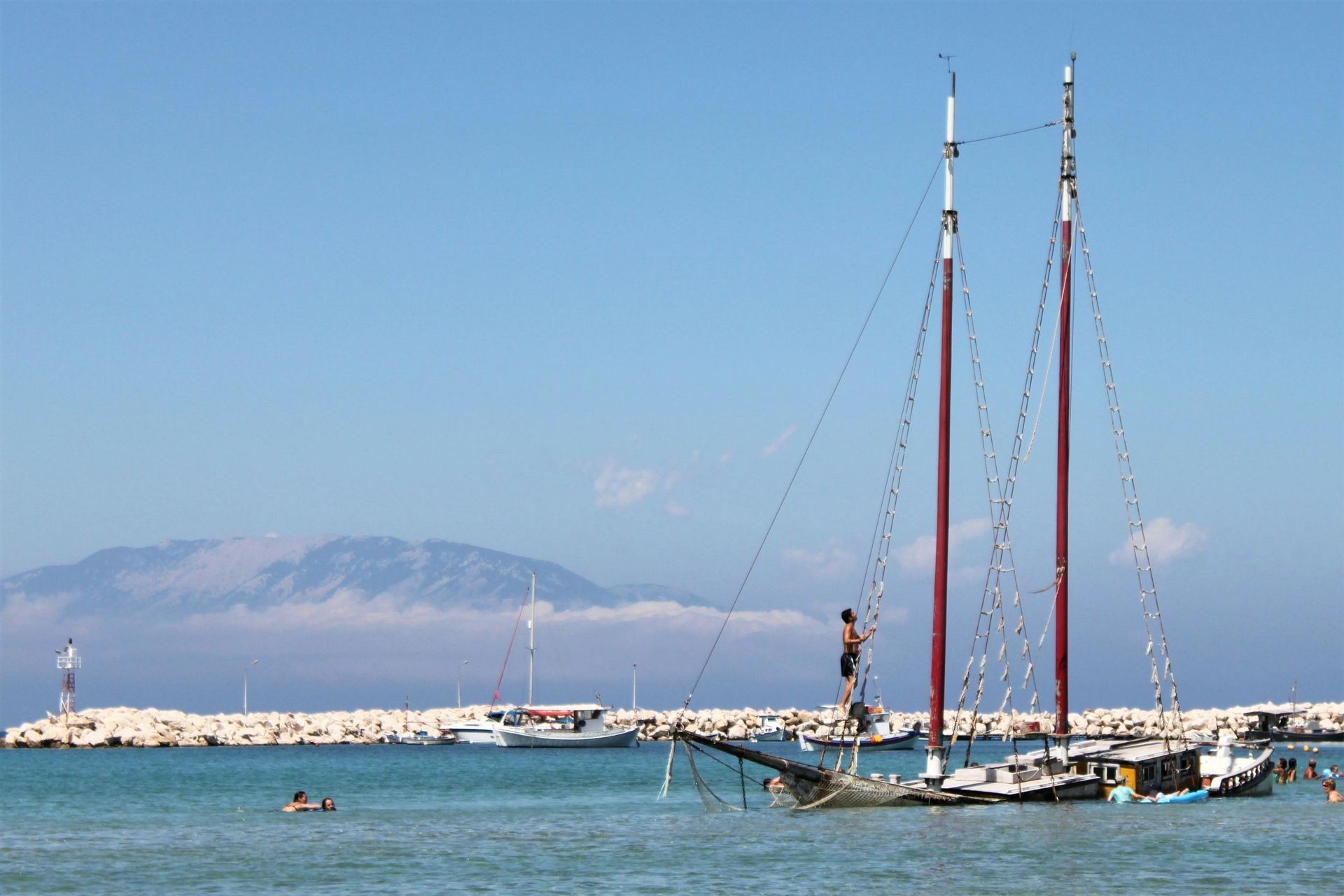 A man is standing on a sailboat in the water in Zakynthos, Greece.