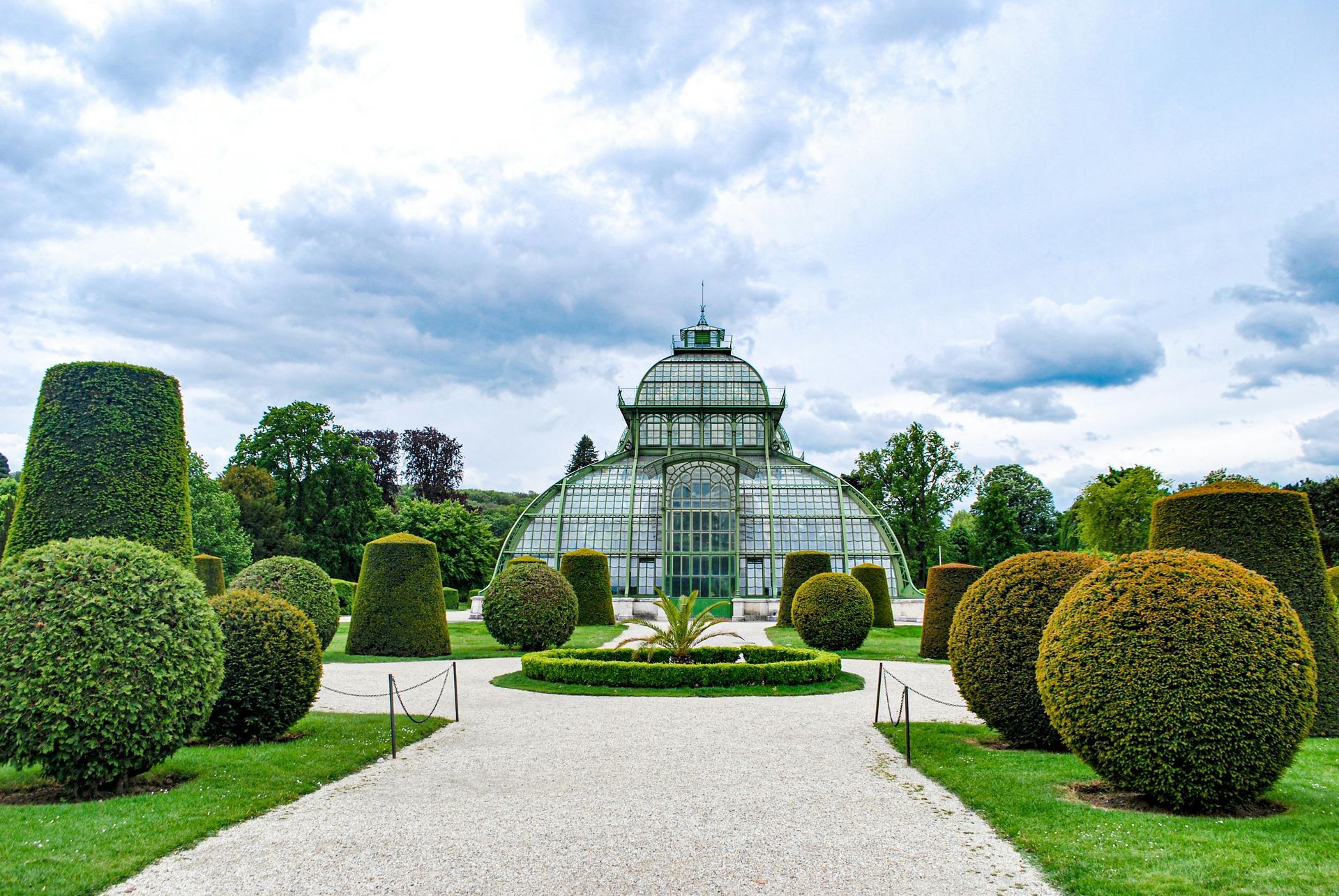 Großes Palmenhaus Schönbrunn is surrounded by bushes and trees in a garden in Vienna, Austria. 