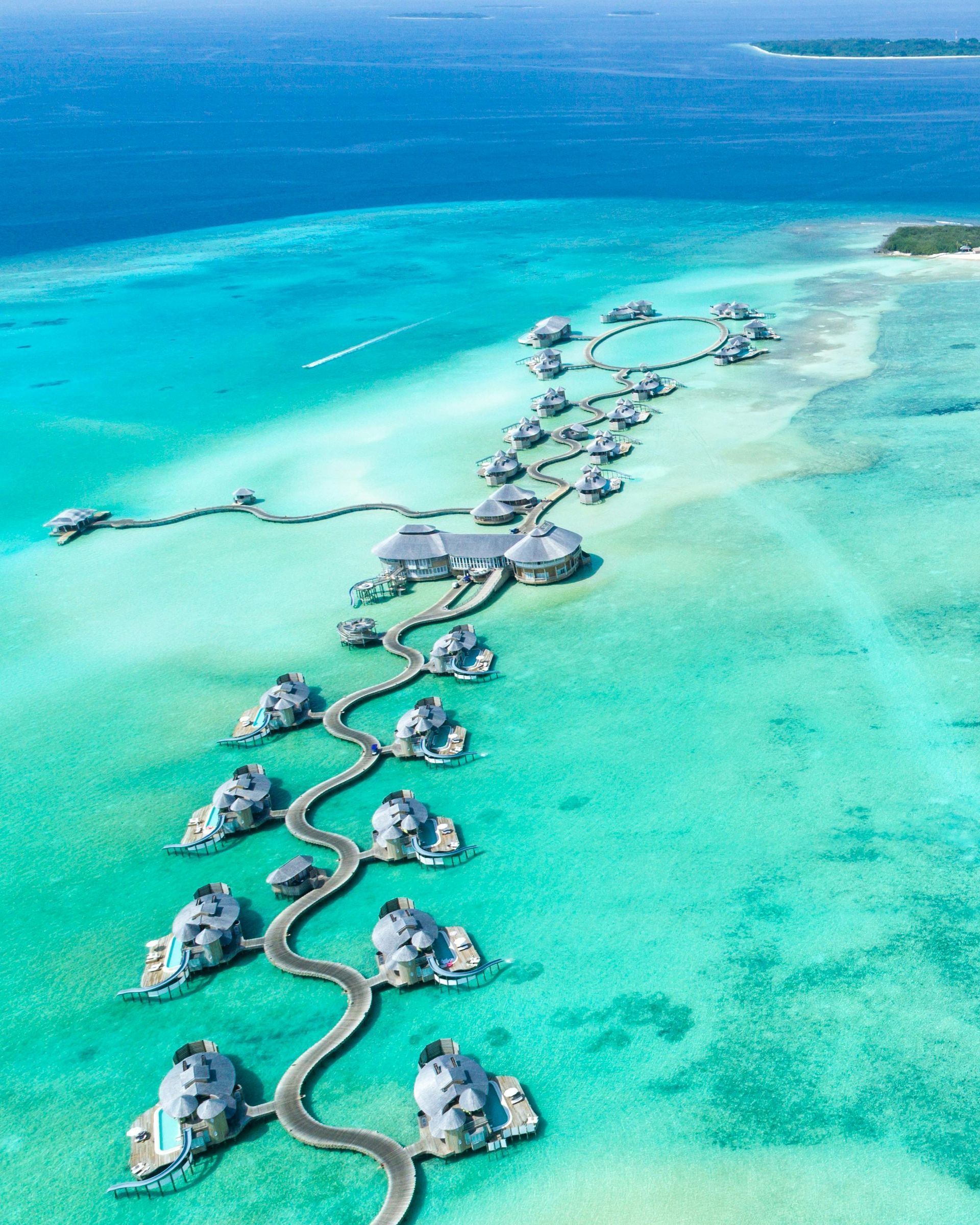 An aerial view of the Cook Islands with a row of over-the-water bungalows in the middle of the ocean.