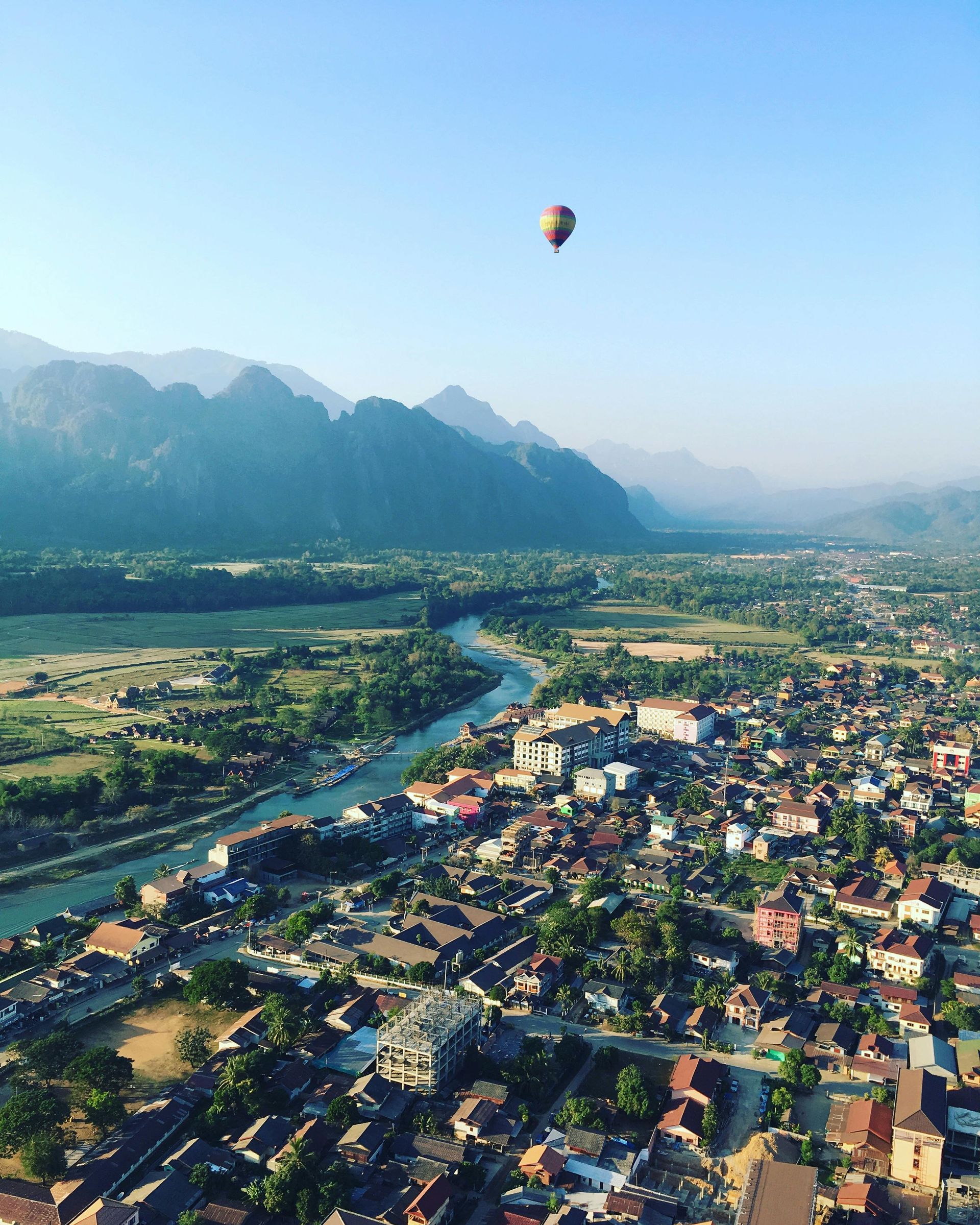 A hot air balloon is flying over a small town with mountains in the background in Laos.