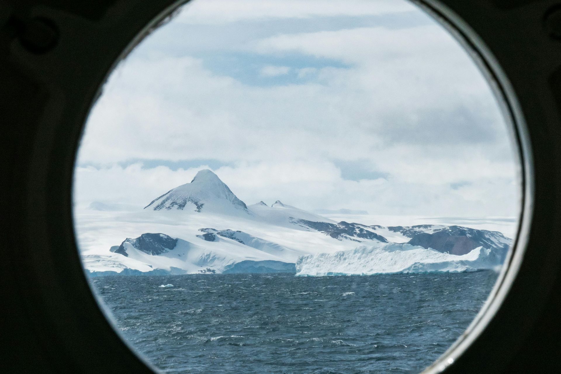 A view of a mountain and icebergs through a round window in Antarctica.