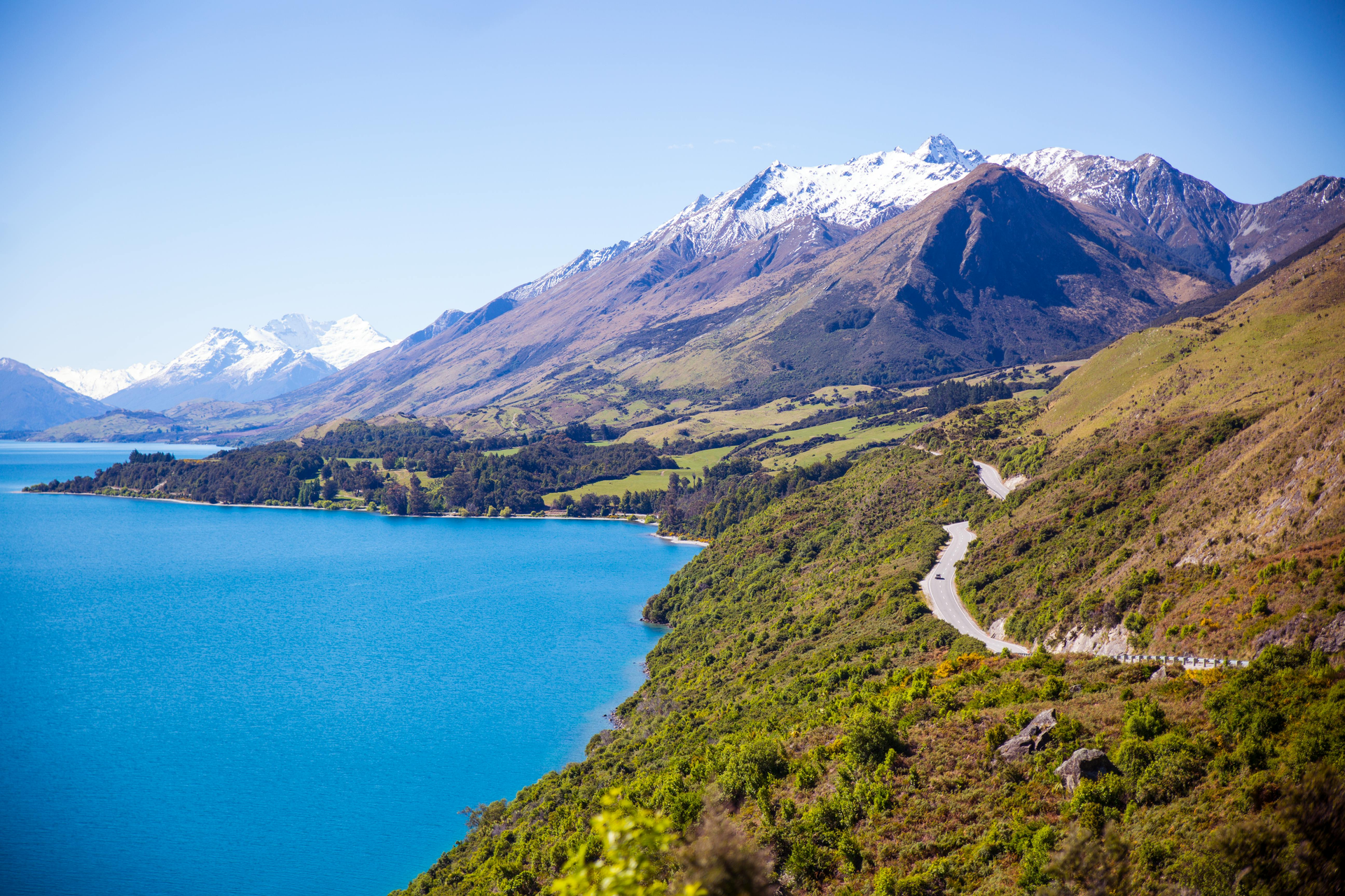 A lake surrounded by mountains and trees with a road going through it in New Zealand.