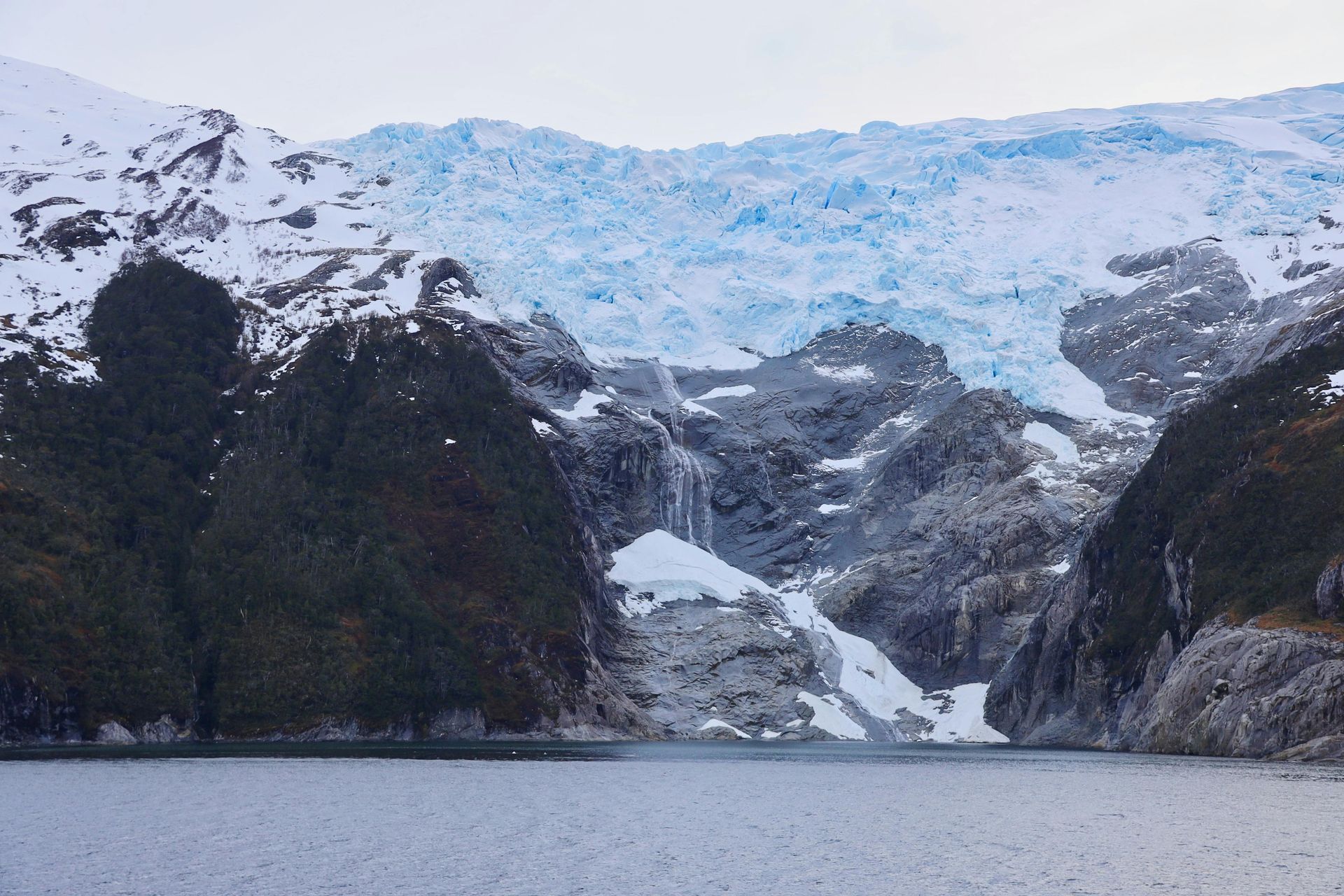 A waterfall in the middle of a lake with mountains in the  backrond  in Antarctica.