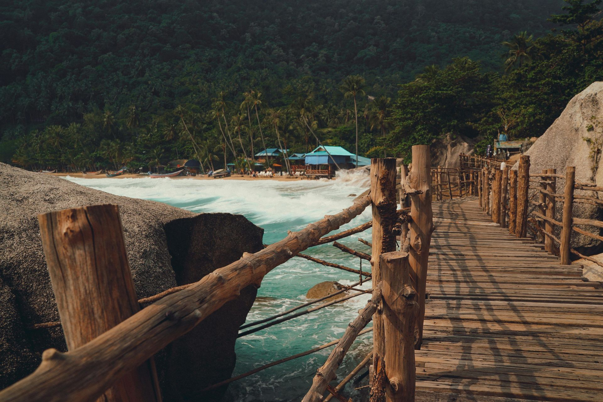 A wooden bridge over a body of water leading to a beach in Thailand.