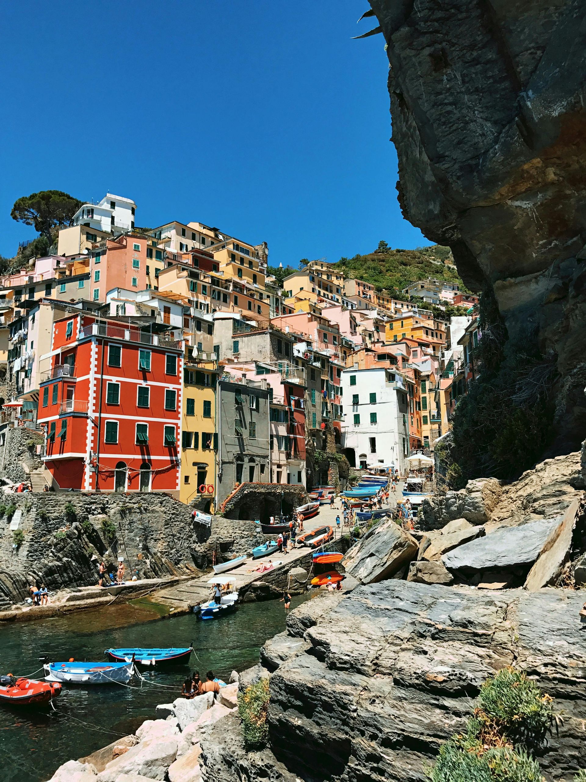 Cinque Terre with boats in the water and a large rock in the foreground in Italy.