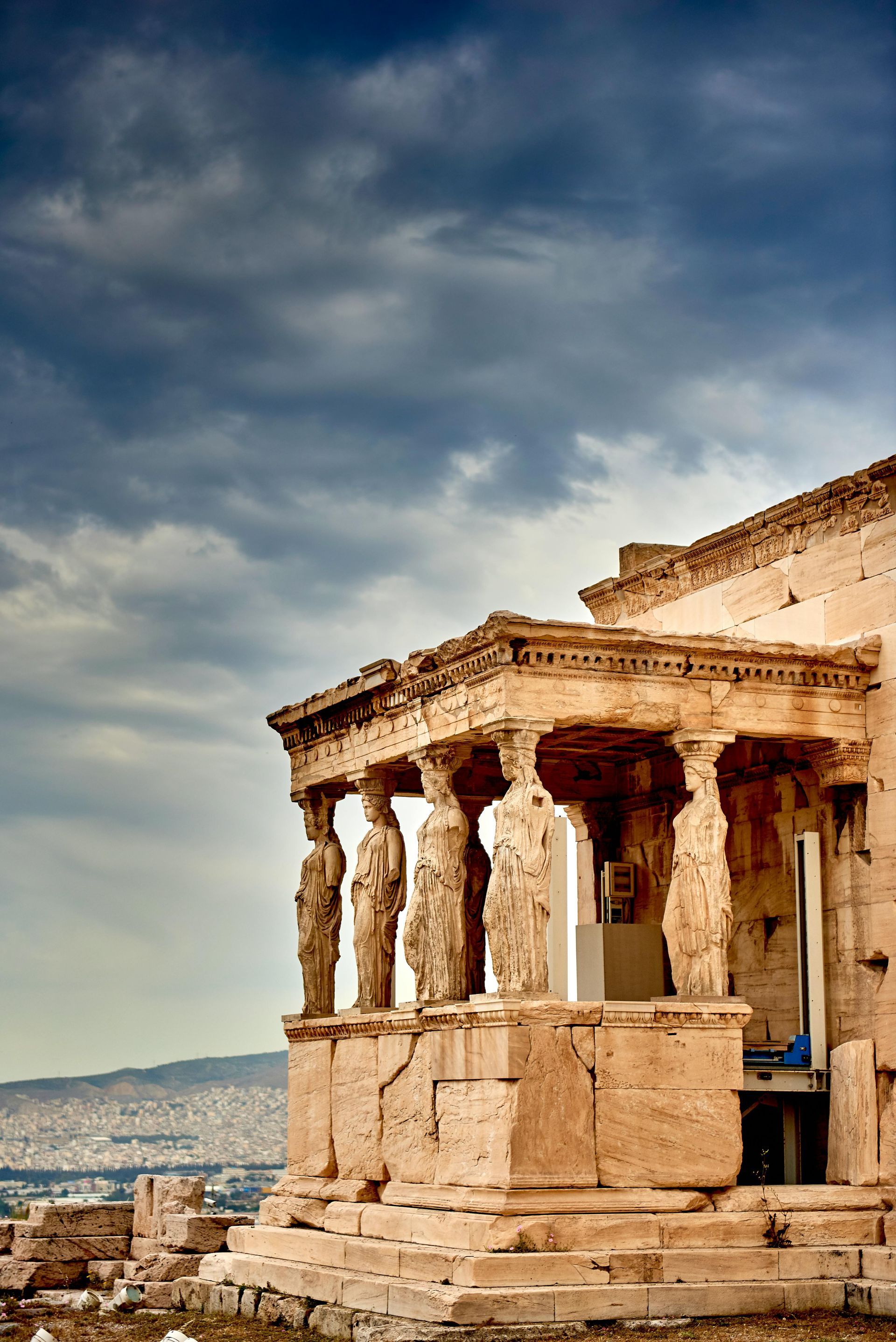 A very old building with columns and statues in front of a cloudy sky in Athens, Greece.