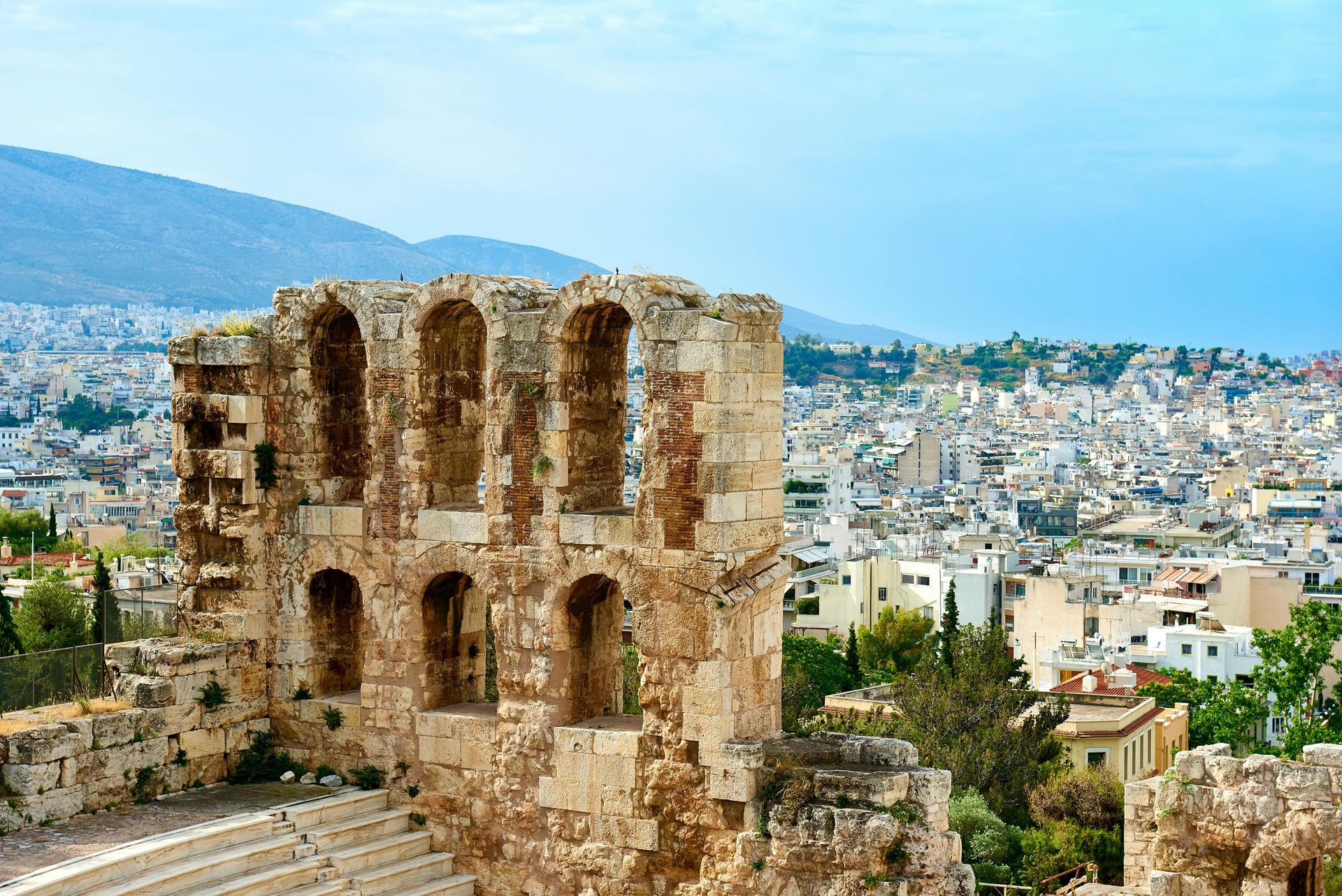 A large stone building with arches in front of a city in Athens, Greece.