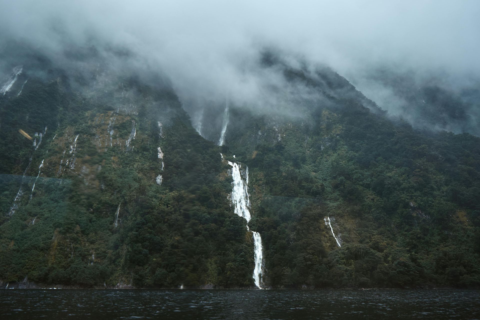 A waterfall is coming down the side of a mountain next to a lake New Zealand.