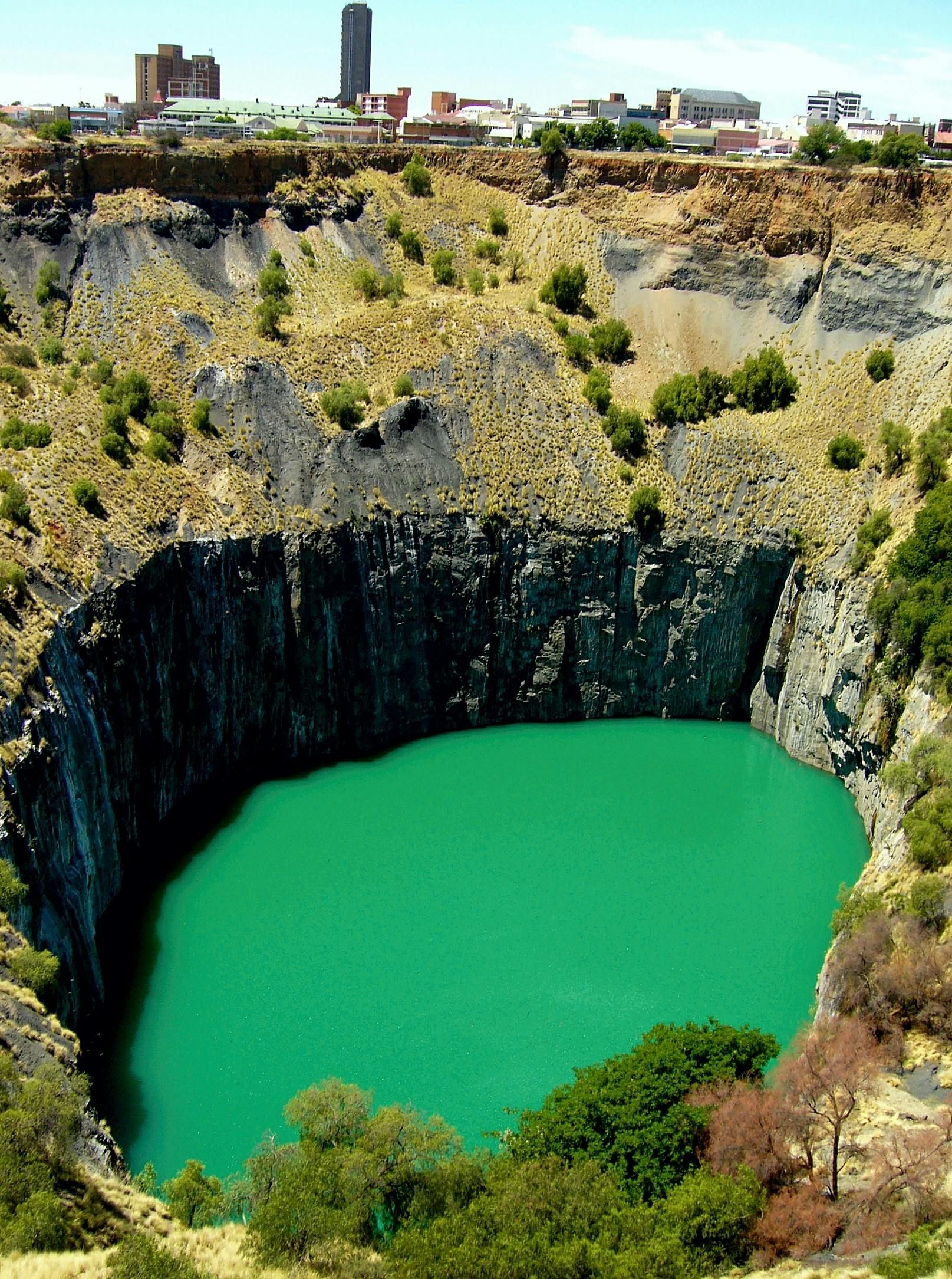 A large hole in the ground with a large green lake in the middle in South Africa.