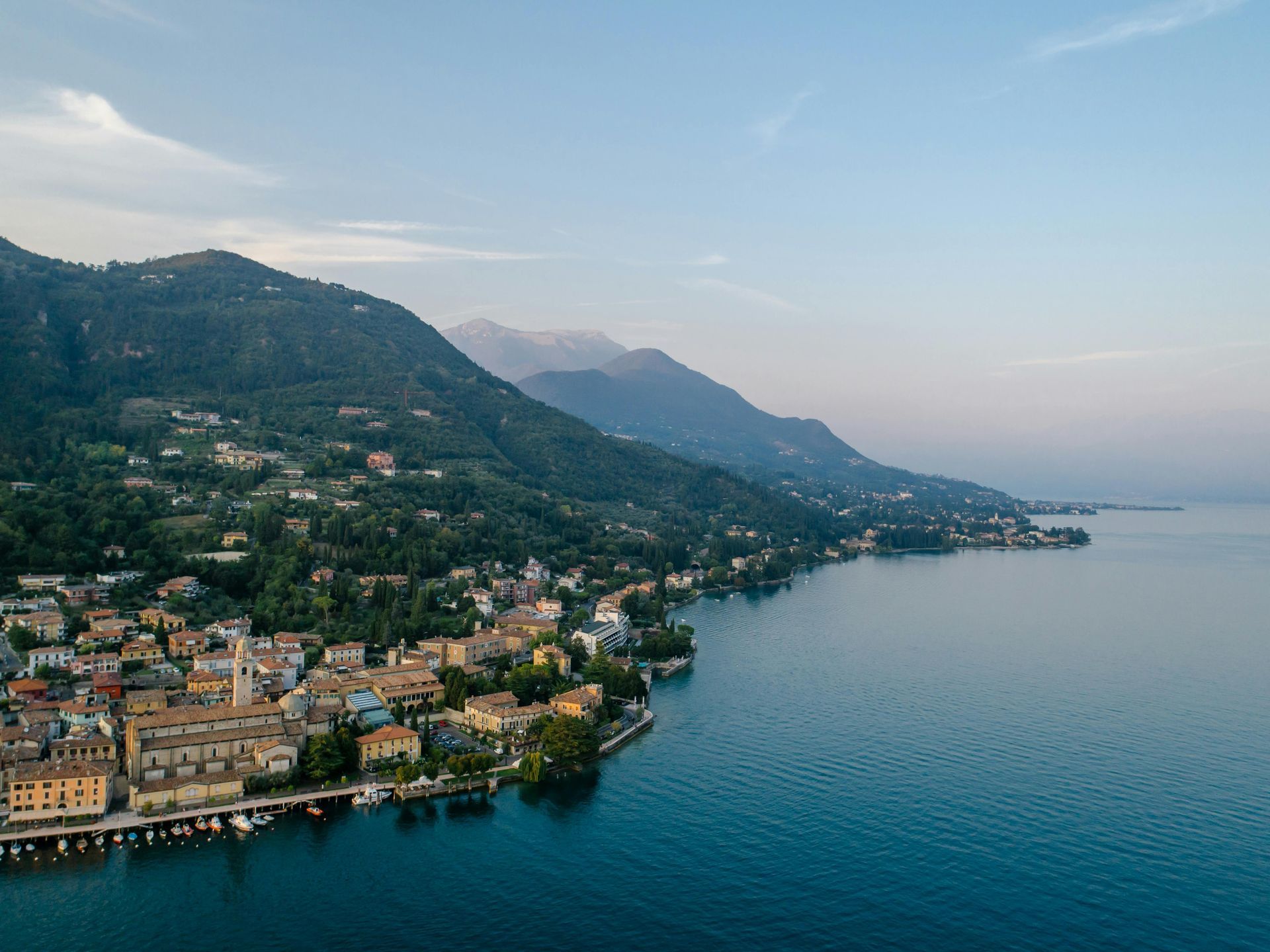 An aerial view of a small town on the shore of Lake Garda surrounded by mountains in Italy.