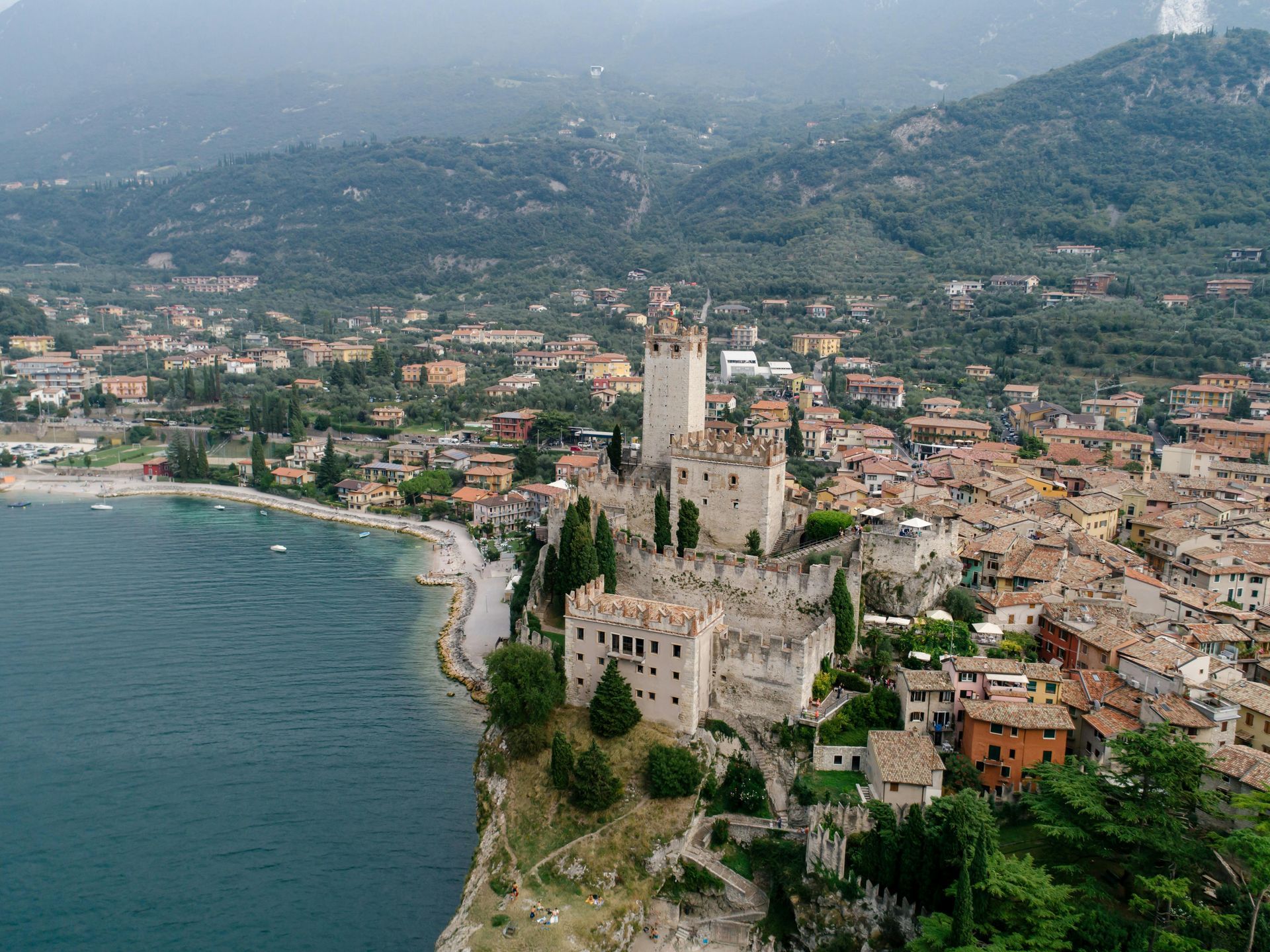 An aerial view of a castle sitting on top of a hill next to Lake Garda, Italy.