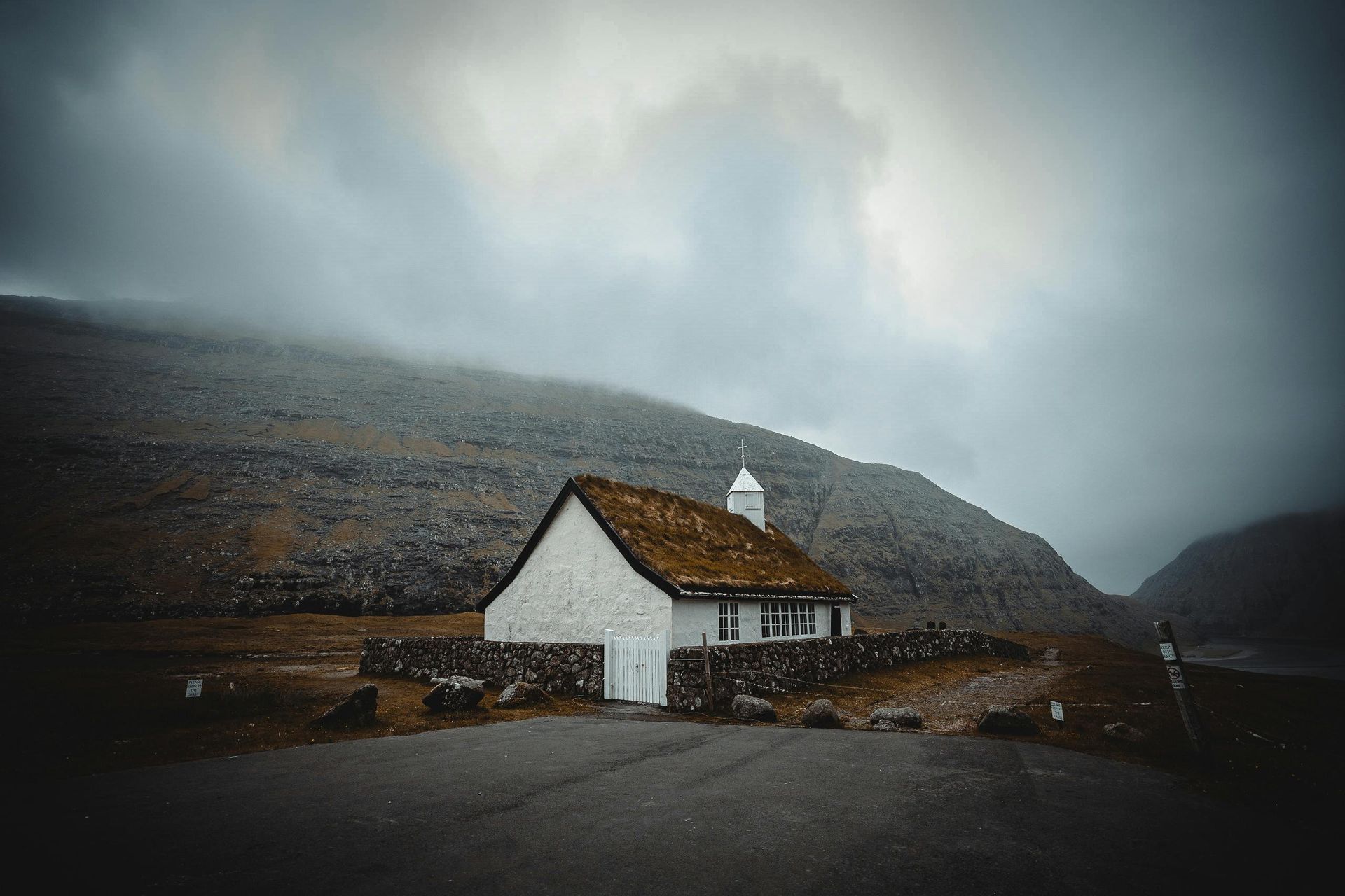 A small white house with a thatched roof is sitting on top of a hill on the Faroe Islands.