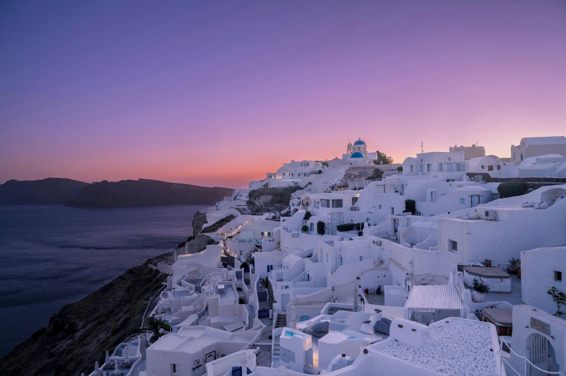 A small white village on a cliff overlooking the ocean at sunset in Santorini, Greece.