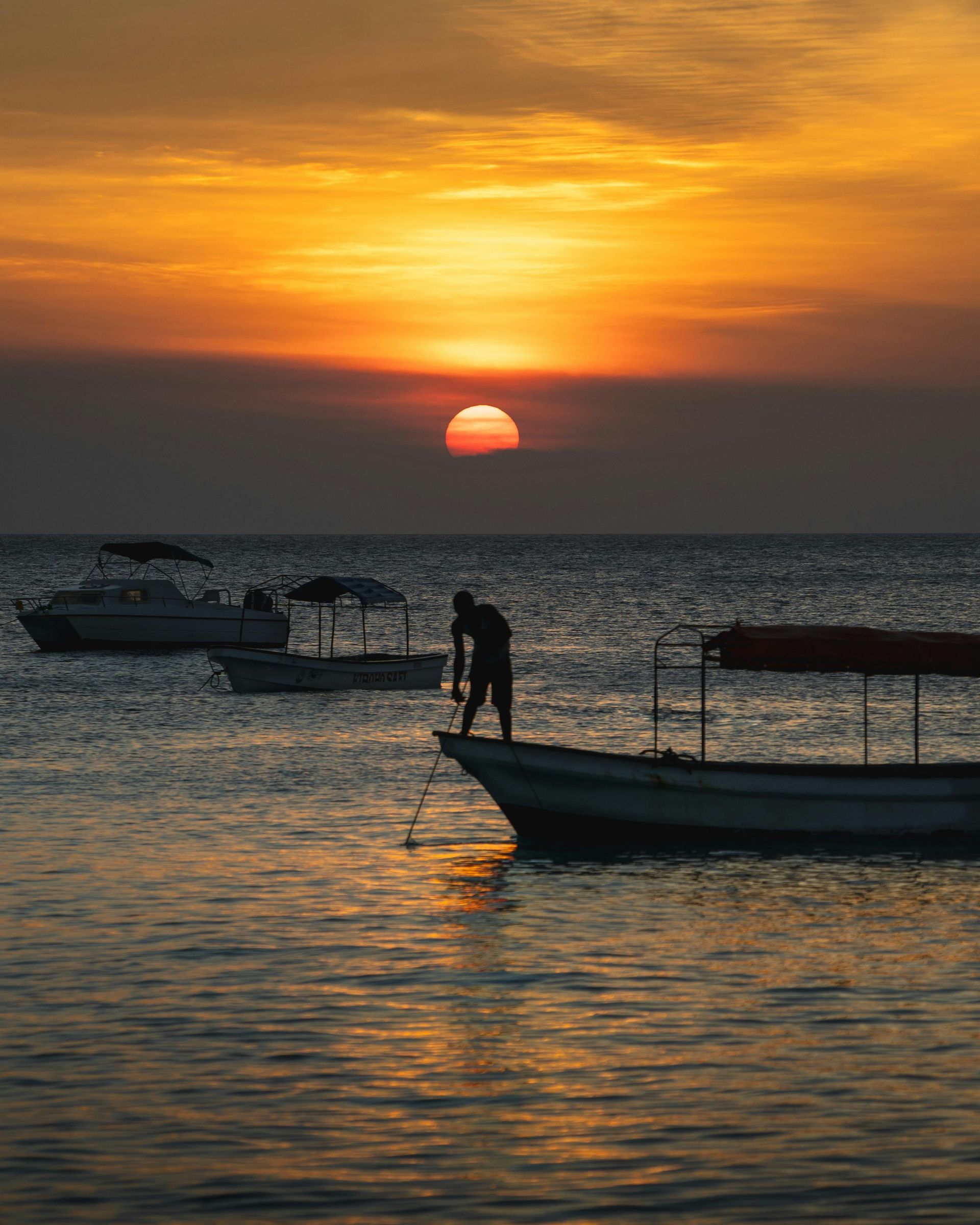 A man is standing on a boat in the ocean at sunset in Tanzania, Africa.