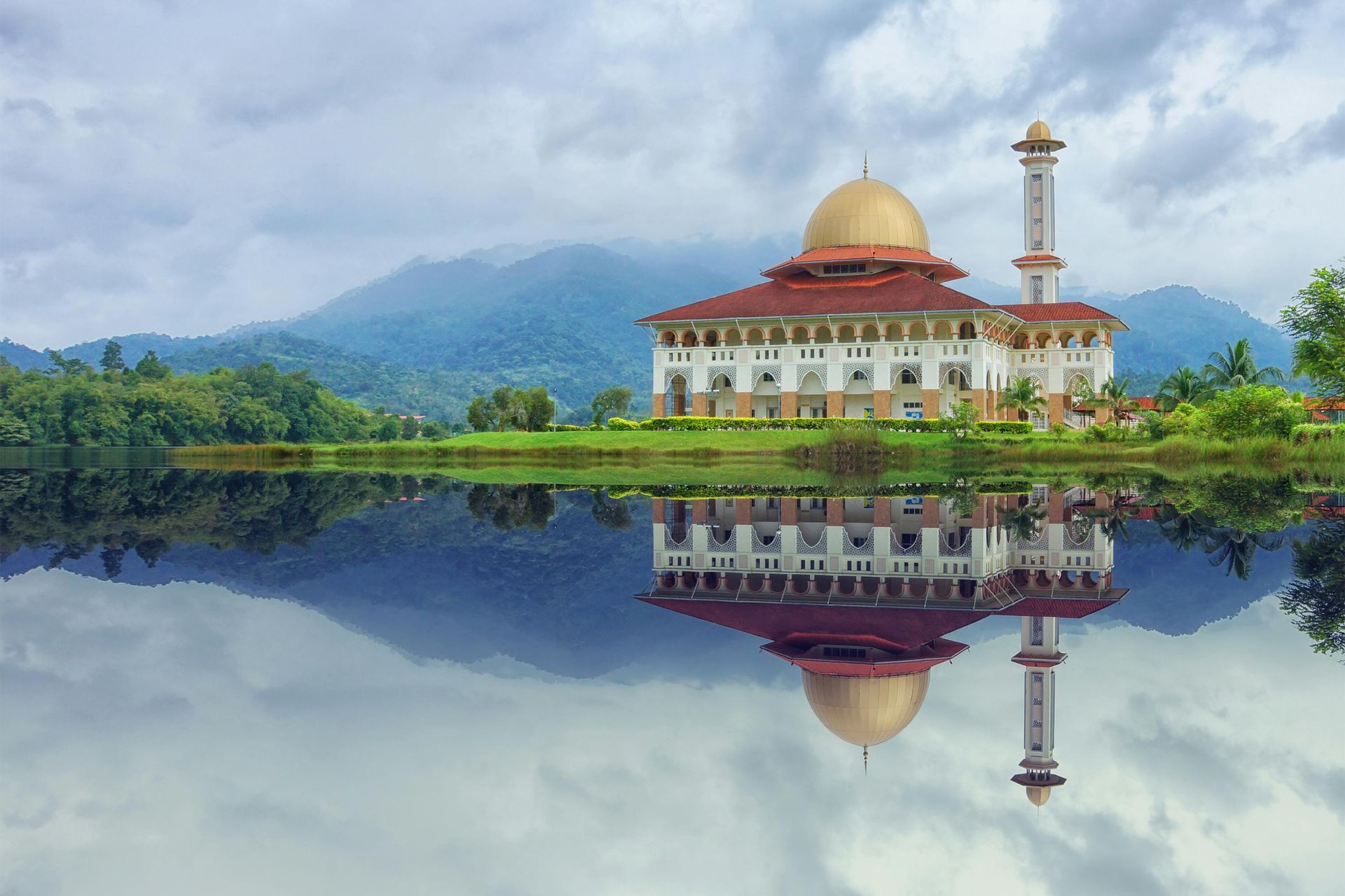 A mosque is reflected in a lake with mountains in the background in Malaysia.