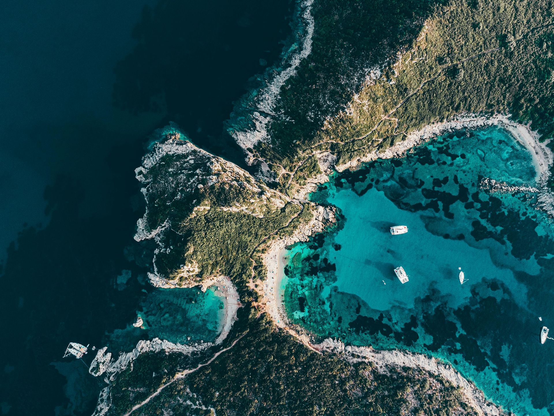 An aerial view of a small island in the middle of the ocean with boats in the water in Corfu, Greece.