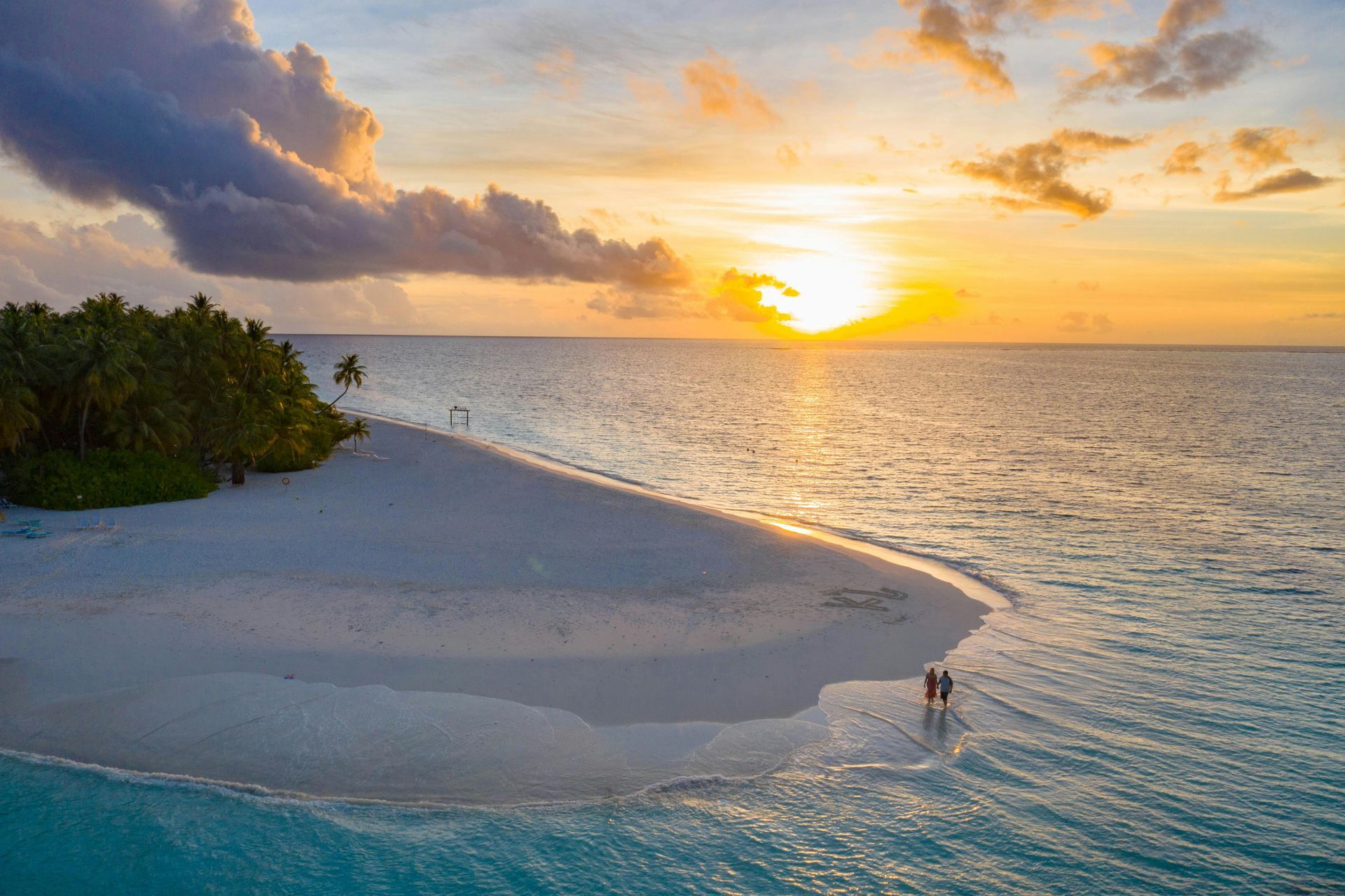 A couple is walking on a sandy beach at sunset in French Polynesia.