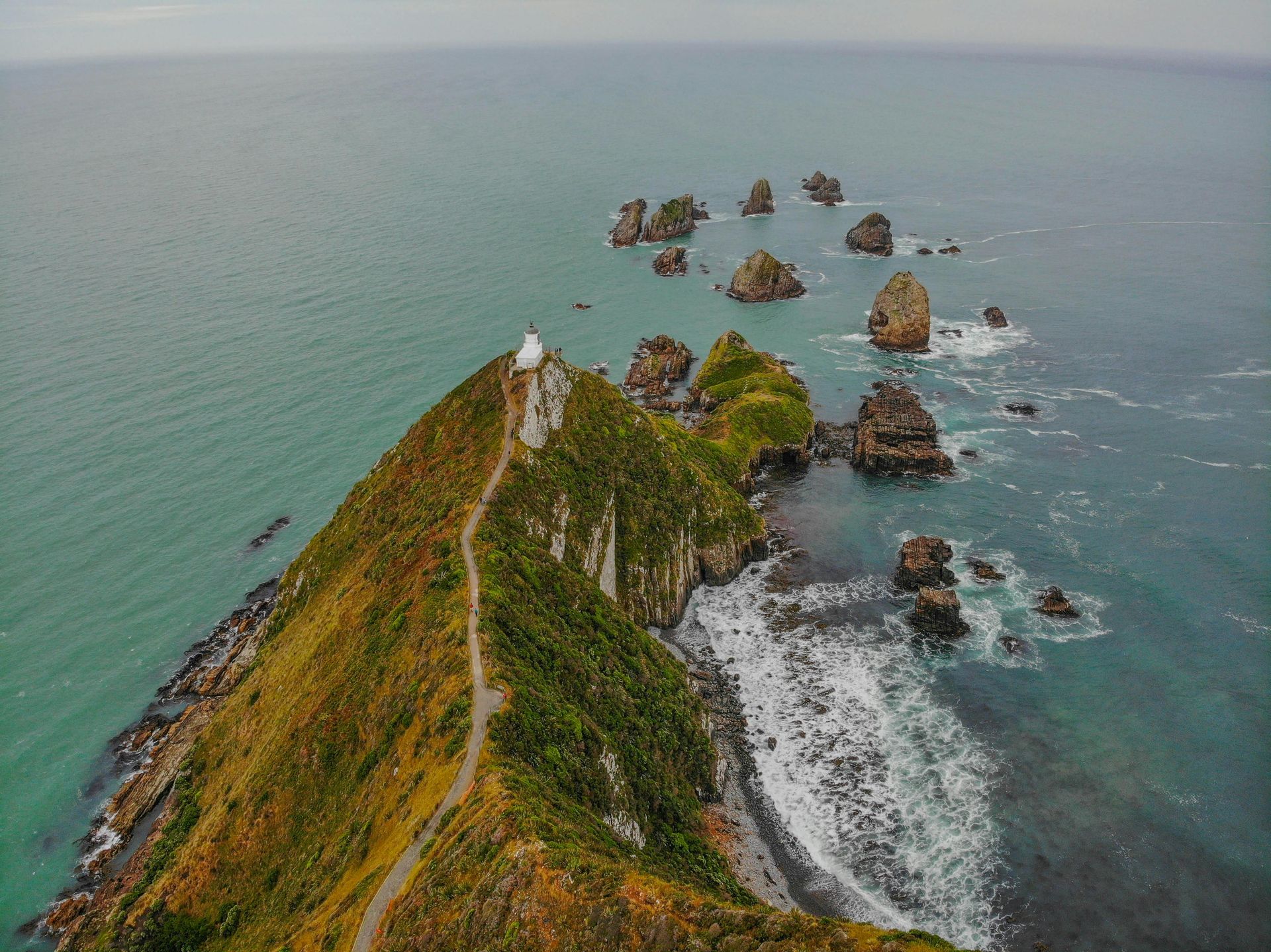 An aerial view of a lighthouse on top of a cliff overlooking the ocean in New Zeland.