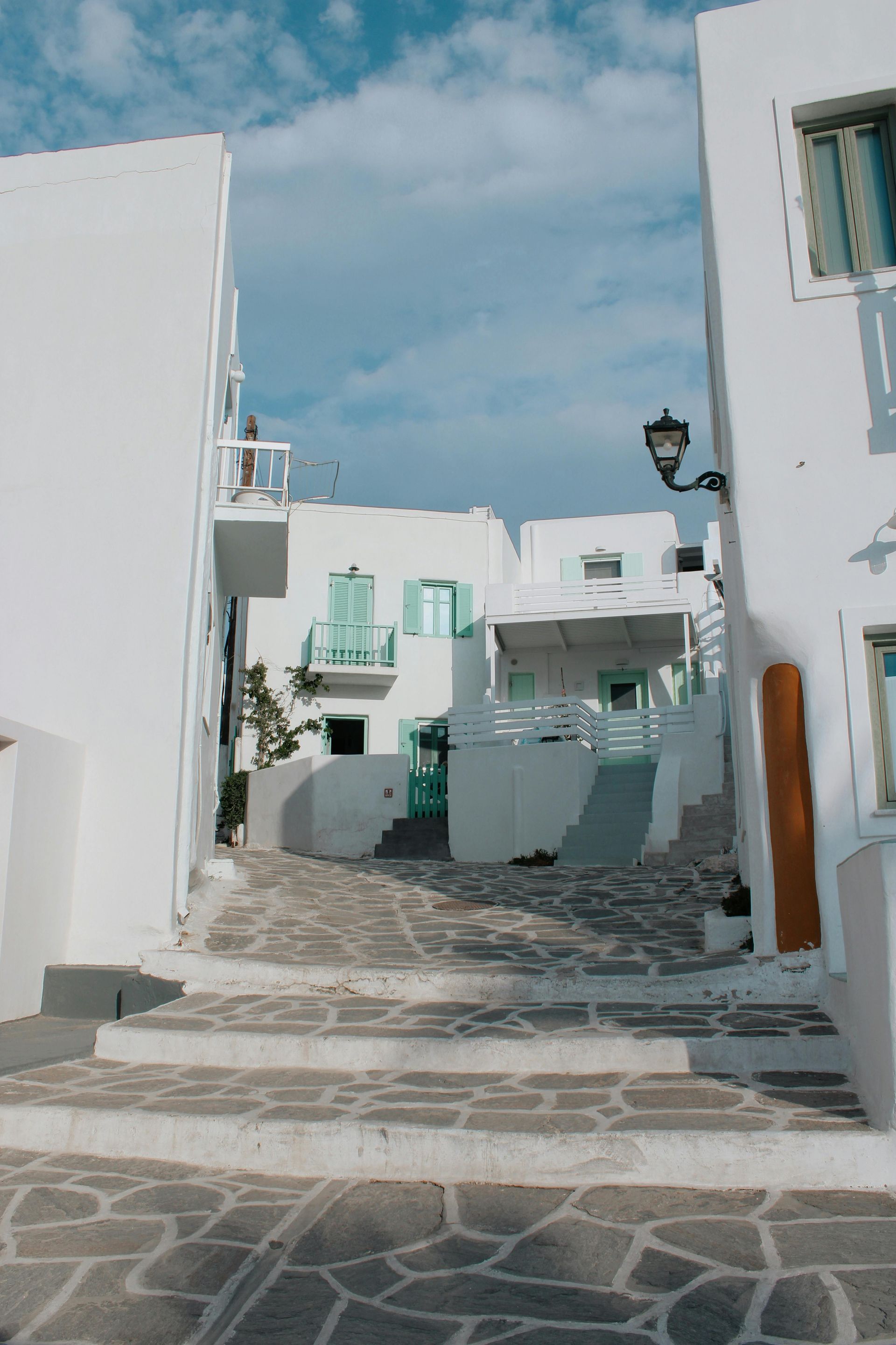 A narrow alleyway between two white buildings with stairs leading up to them in Paros, Greece.