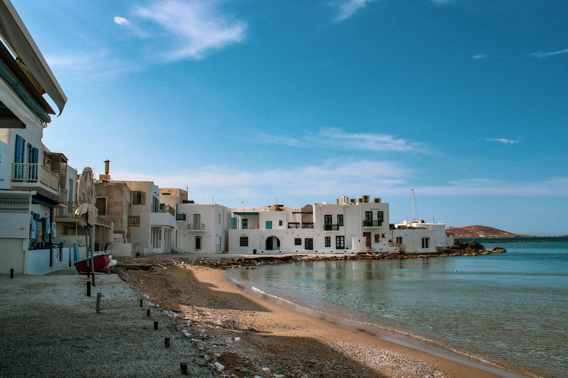 A beach with buildings on the shore and a boat in the water in Paros, Greece.